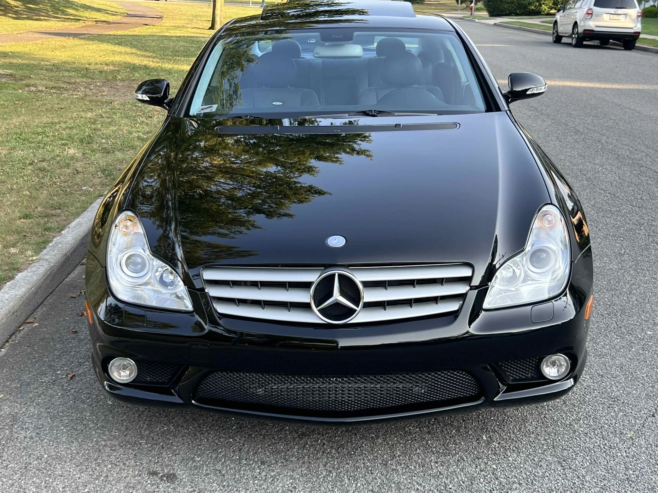 Black Mercedes-Benz car parked on a residential street with trees and other vehicles in the background.