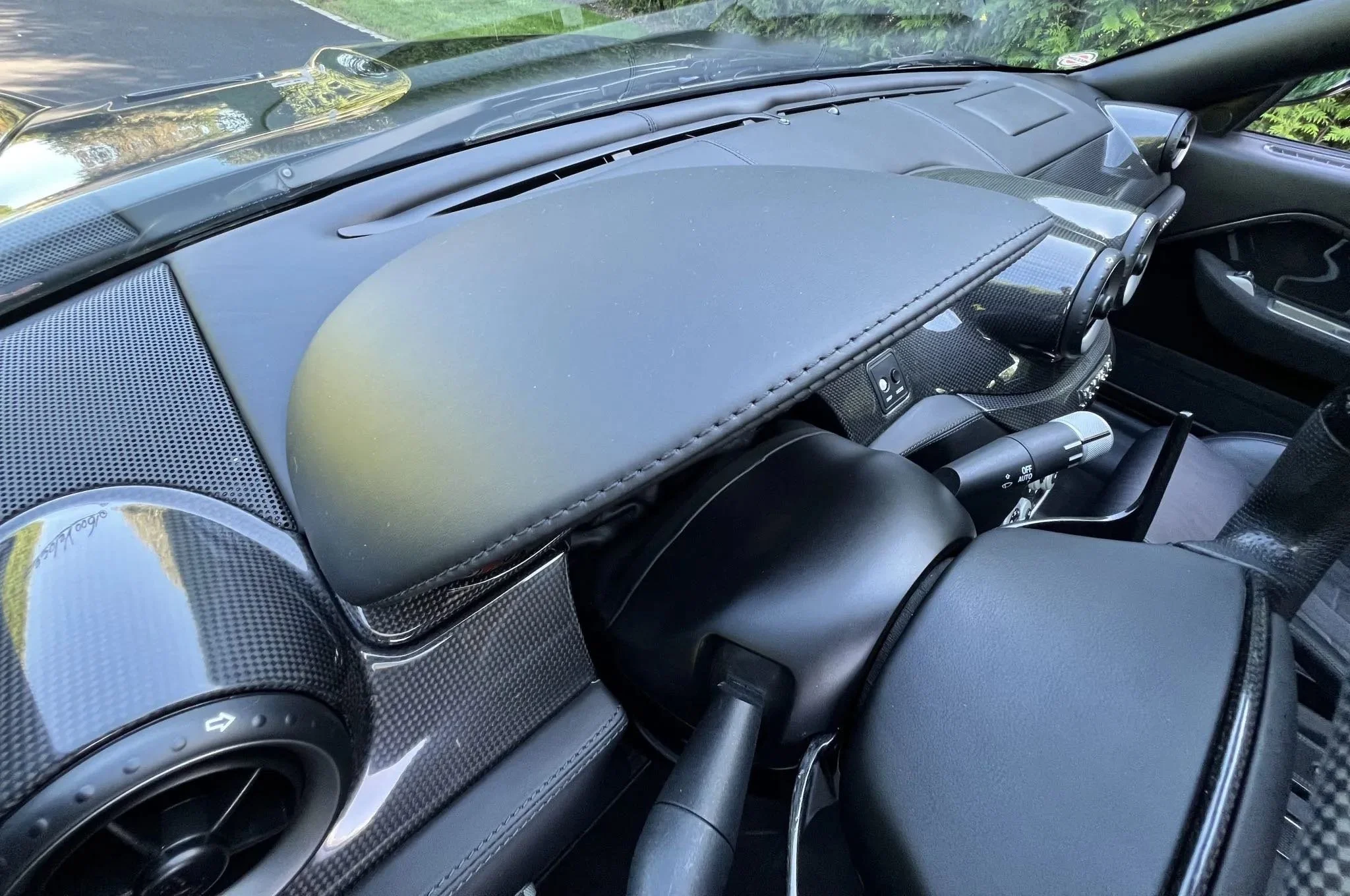 Interior of a sports car with carbon fiber dashboard, black leather seats, and visible controls and air vents.