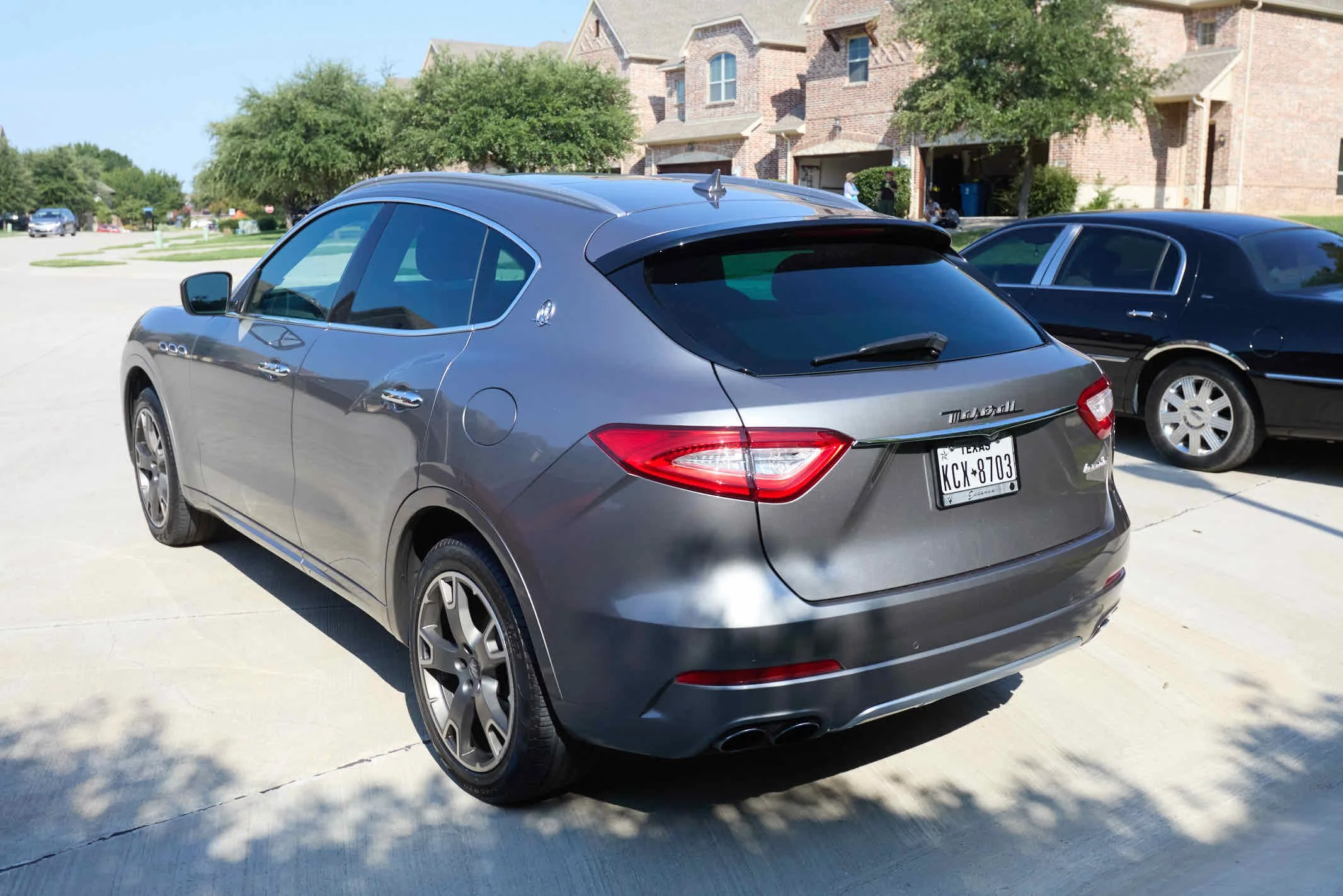 Gray Maserati Levante parked in a driveway with houses and trees in the background.