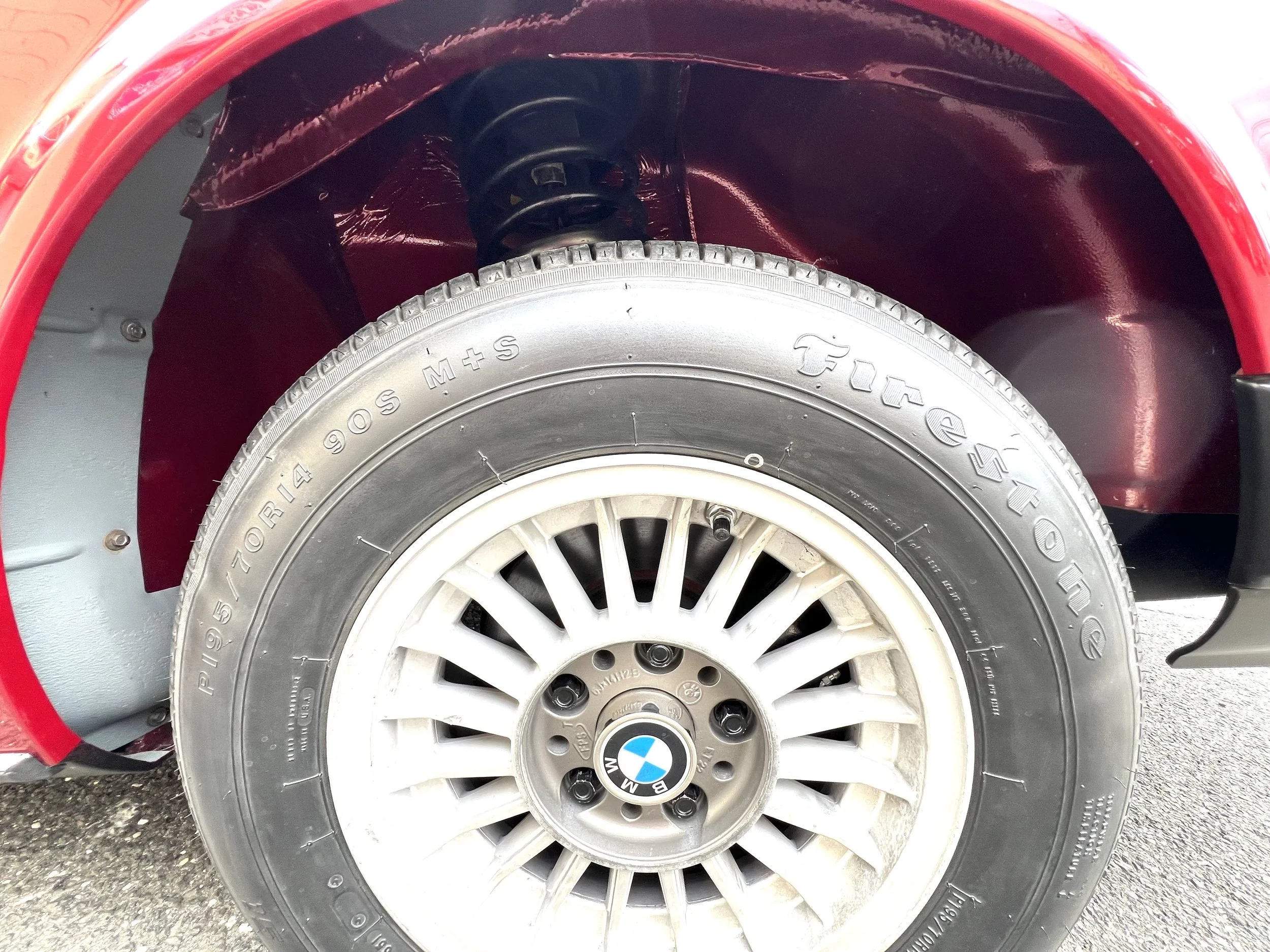 Close-up of a BMW BMW 630 csi car wheel with a tire marked 'P195/70R14 90S'. The wheel rim is white with BMW logo at the center, and the wheel well is painted red.