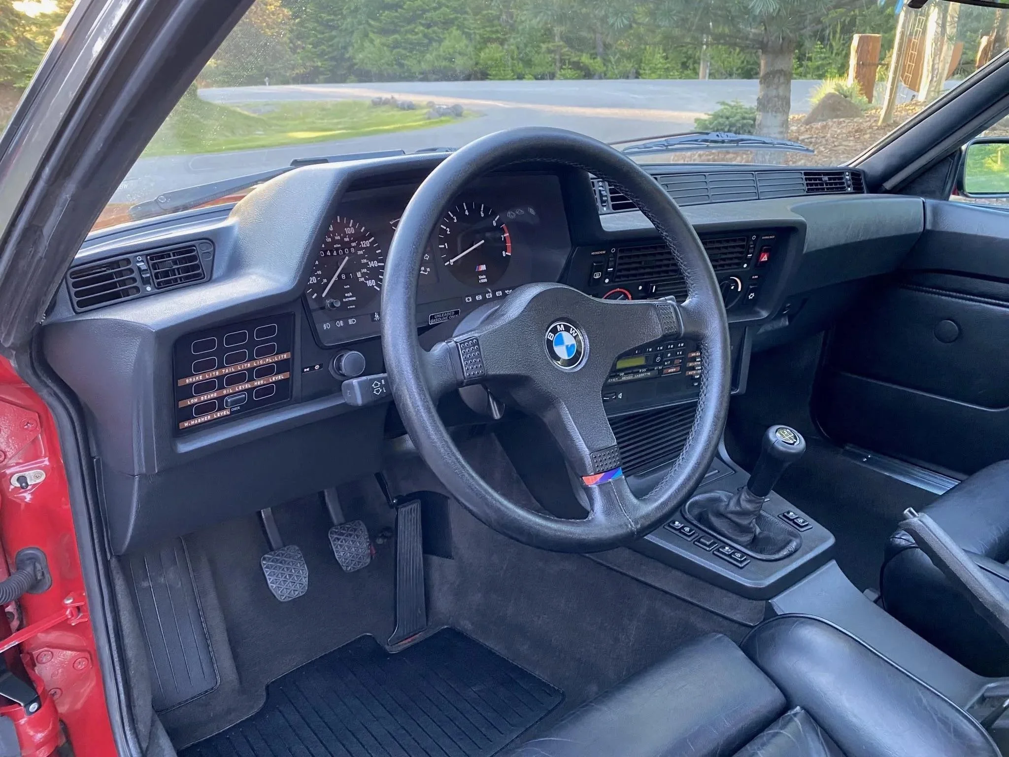 Interior of a vintage BMW car, showing the steering wheel, dashboard with speedometer and tachometer, gear shift, and black leather seats.