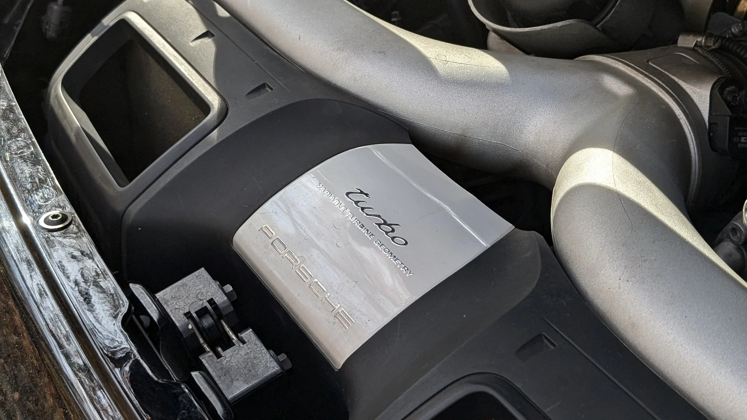 Engine bay of a Porsche Turbo with a silver label that reads Turbo and says Variable Adaptive Geometry, with visible engine components, including air intake and manifold.