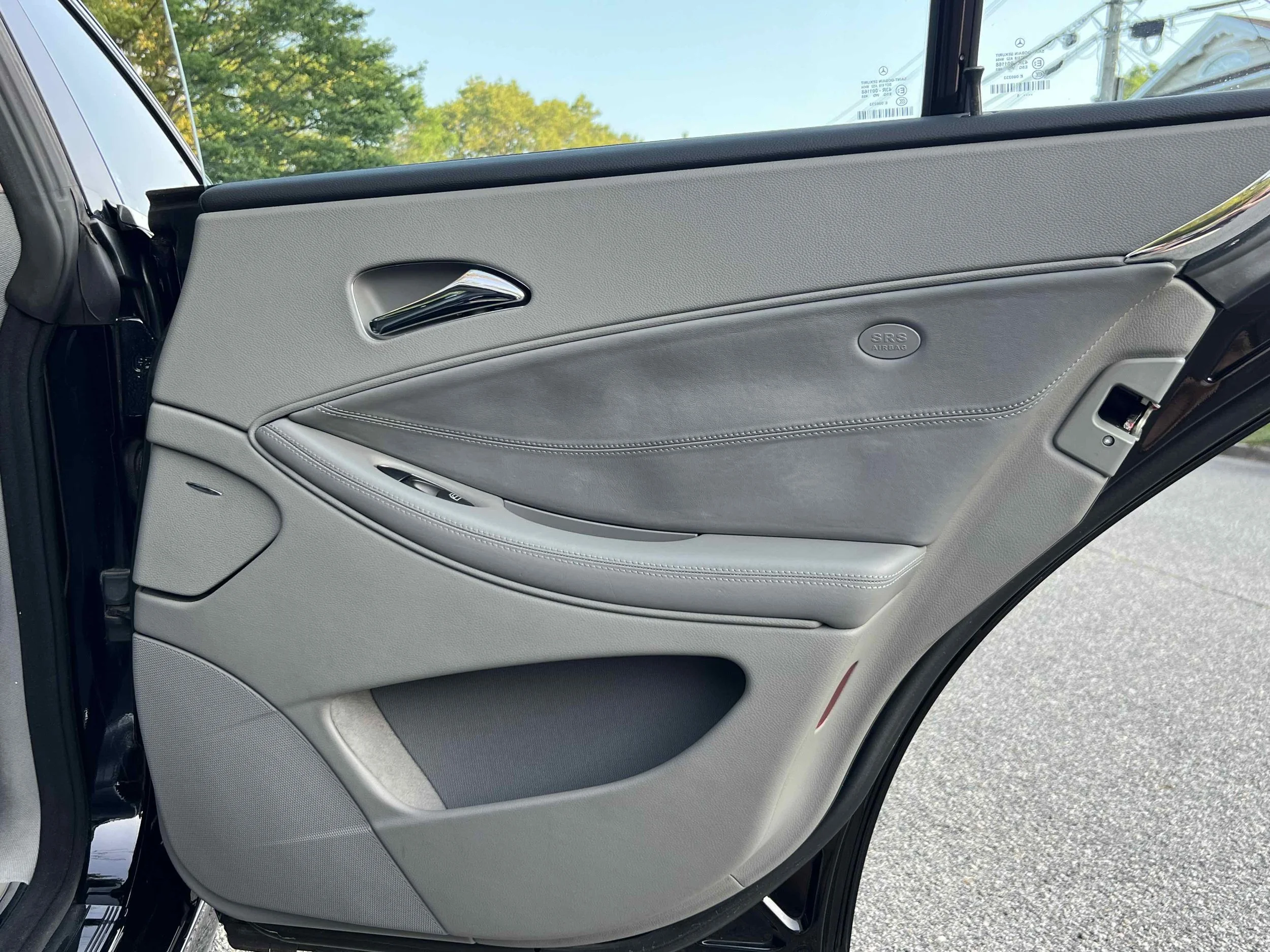 Close-up of a car door interior featuring gray and black upholstery, chrome door handle, window controls, and an SRS airbag label.