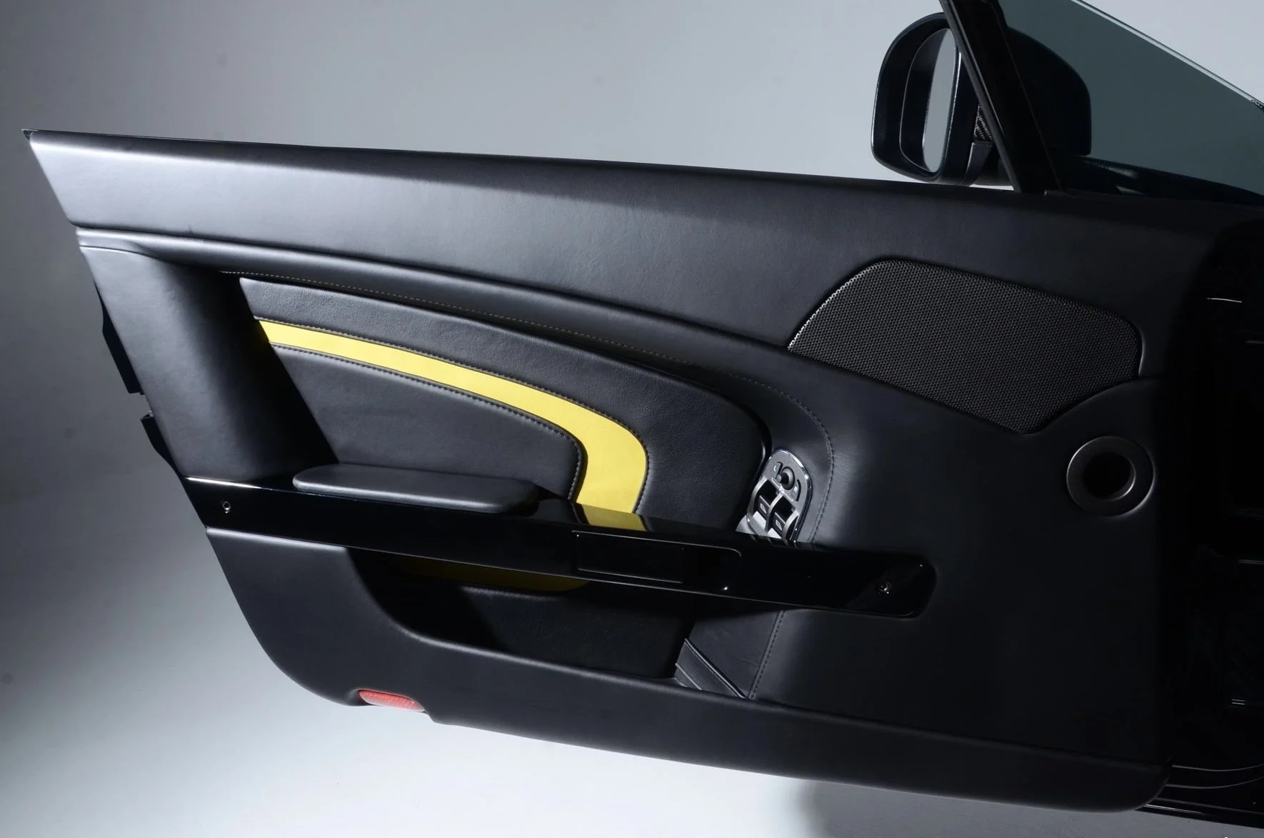 Close-up of a modern car door interior with black and yellow accents, a speaker, and control buttons.