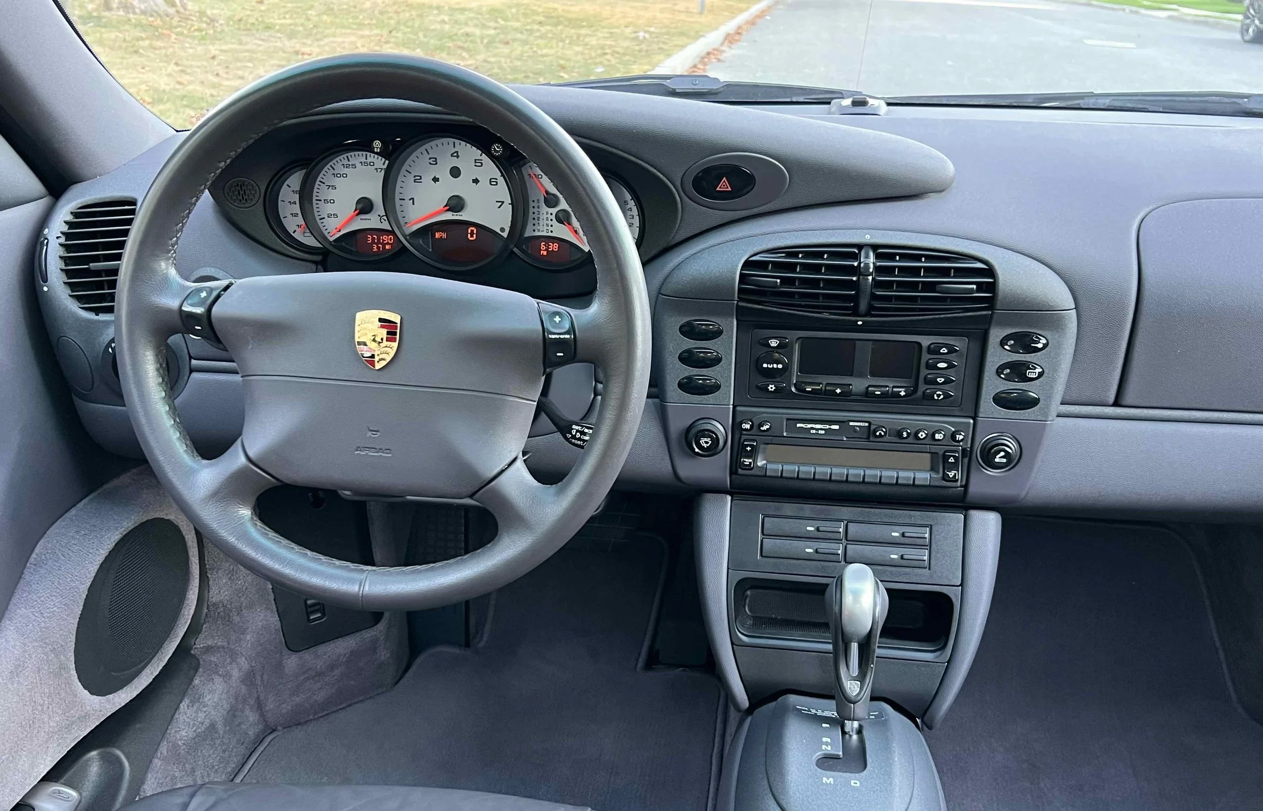The interior dashboard of a Porsche sports car with a leather steering wheel, analog gauges, and center console controls.