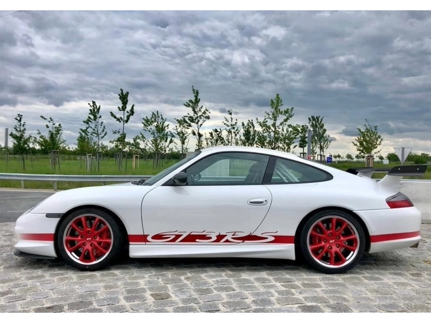 2004 Porsche 911 GT3 RS with red graphics on a cobblestone street with trees in the background under a gray sky