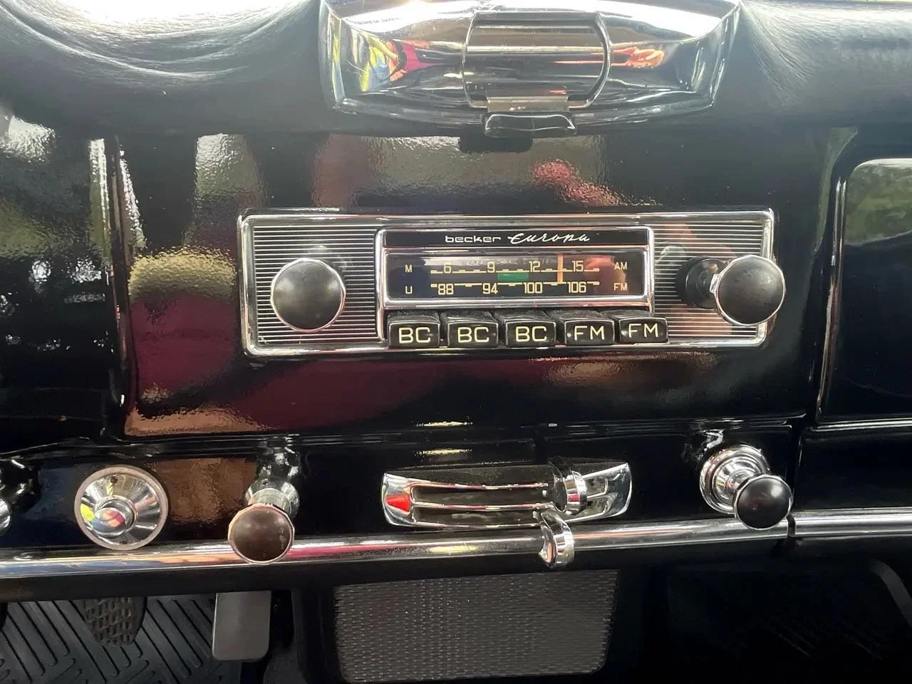 Dashboard of a vintage Becker Europa car radio with control knobs and frequency display, set in a classic black car interior.