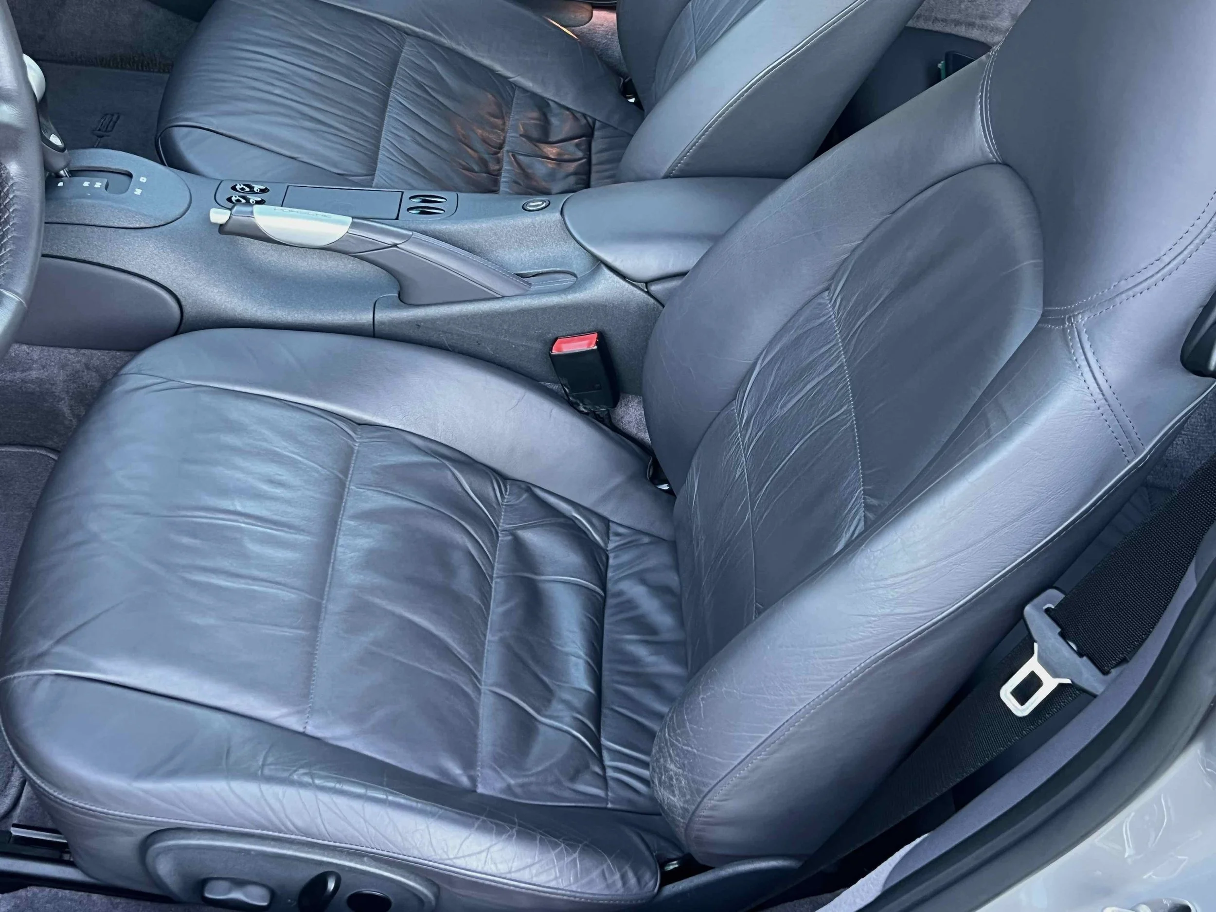 Front interior of a car showing black leather driver and passenger seats, center console with gear shift, and seatbelt.