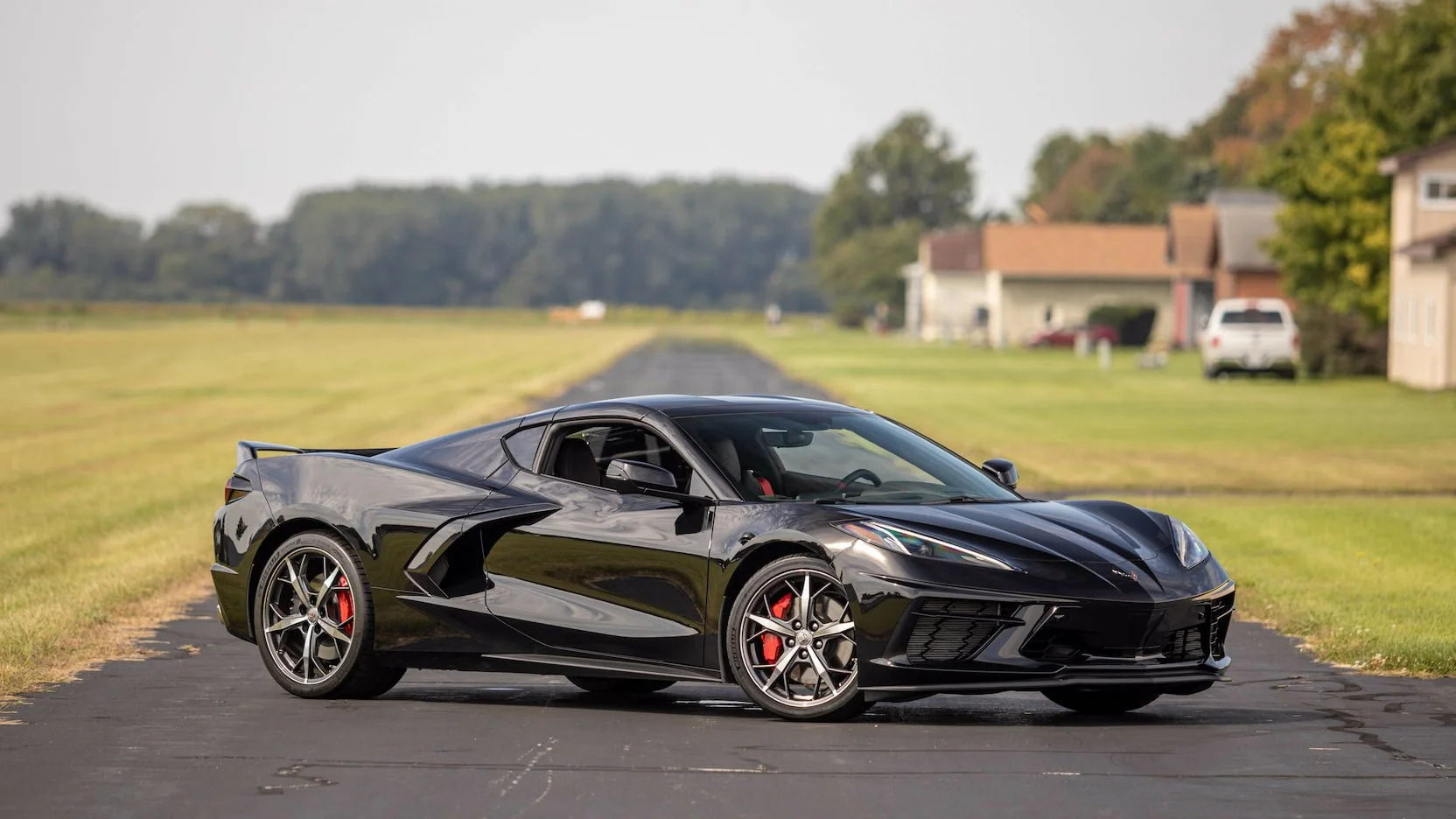 Black Chevrolet Corvette sports car parked on a paved road in a suburban neighborhood.