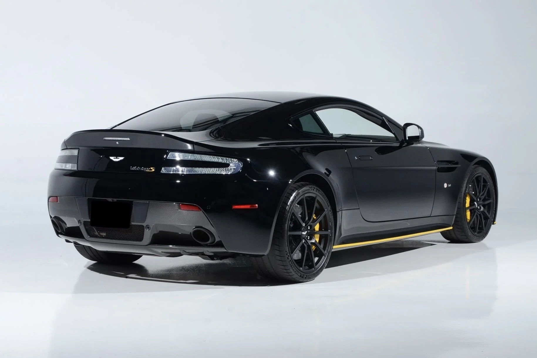 A sleek black sports car with yellow accents, parked on a plain white background, viewed from the side and rear.