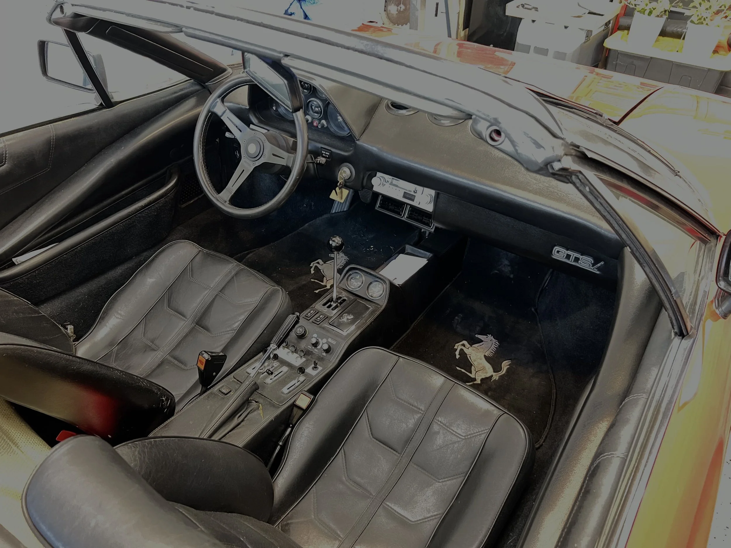 Interior of a classic Ferrari GTS/LM sports car with black leather seats featuring the Ferrari logo, a manual gear shift, and a dashboard with gauges and controls.