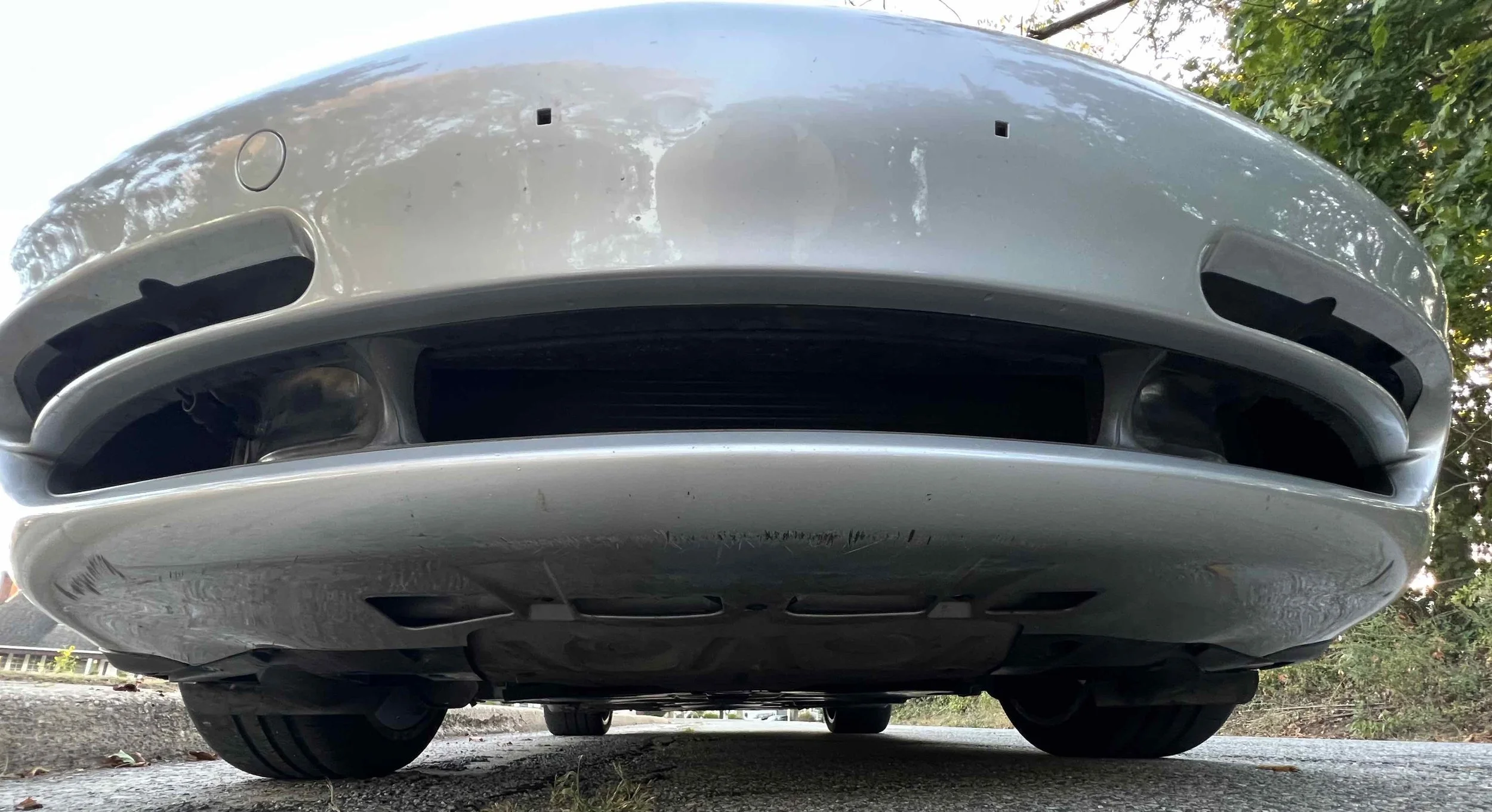 Close-up of the front underside of a silver car, showing the grille, air intakes, tires, and part of the bumper.