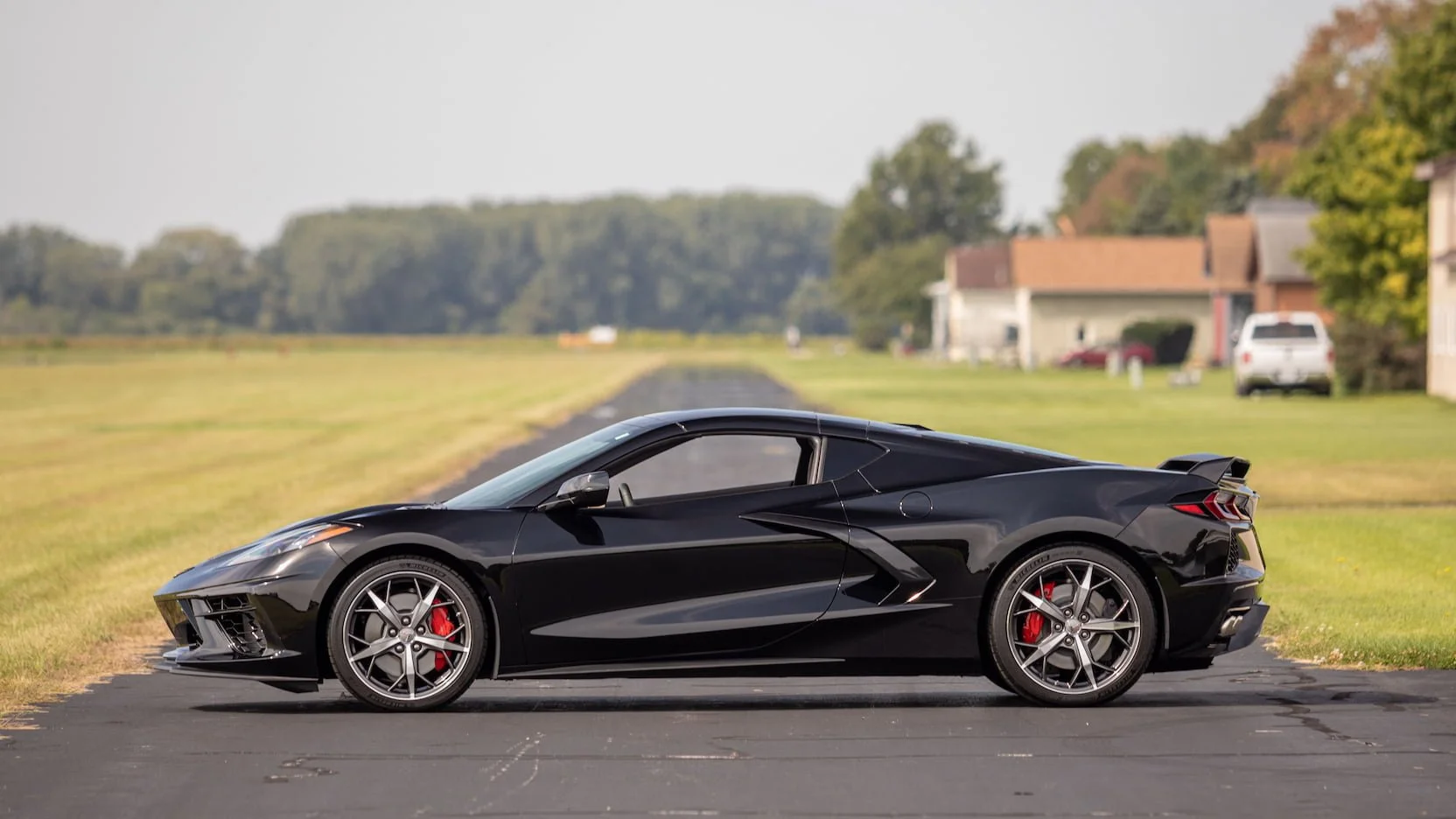 Black sports car parked on a paved road with houses and trees in the background.