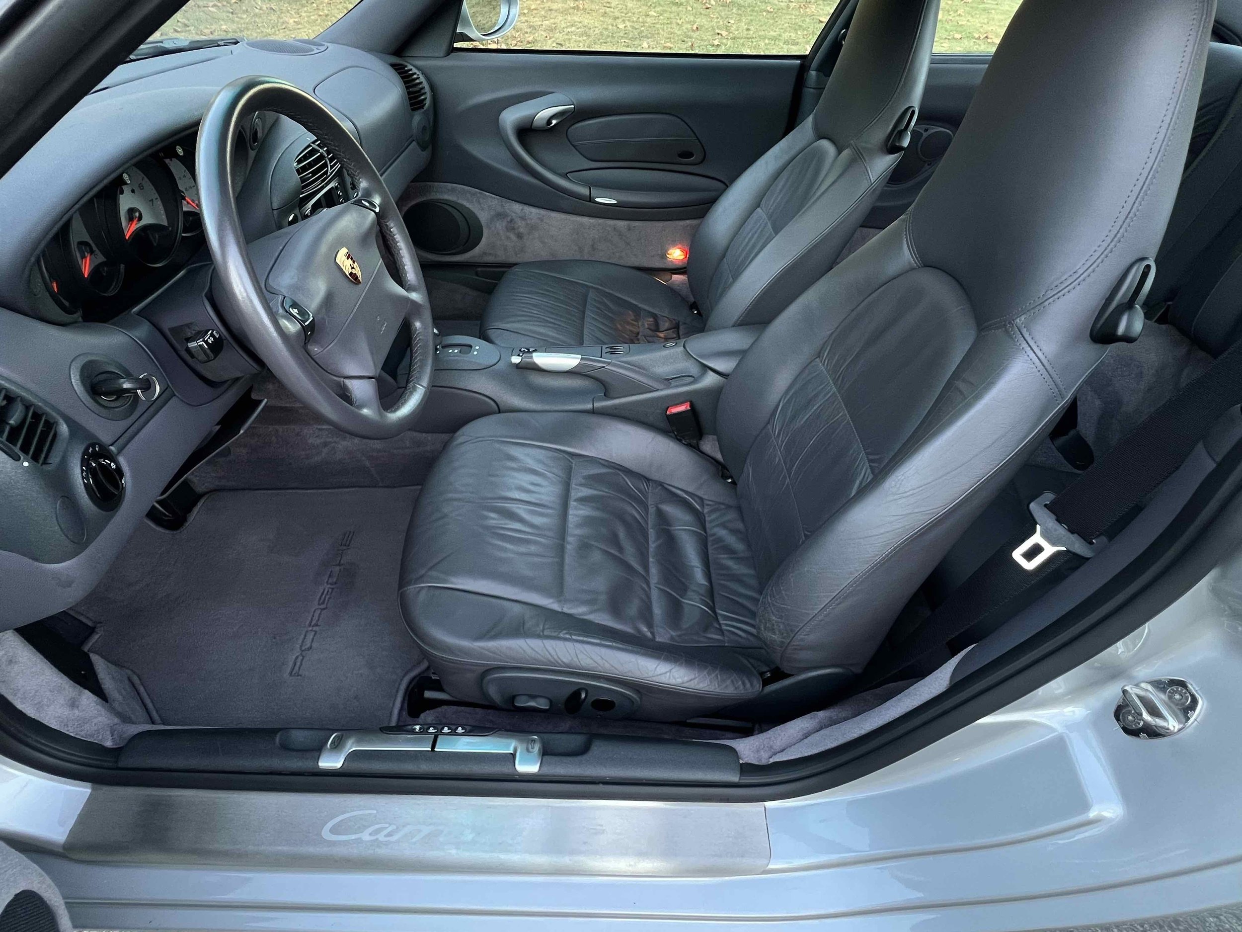 Interior of a silver Porsche car showing black leather seats, dashboard, steering wheel, and center console.