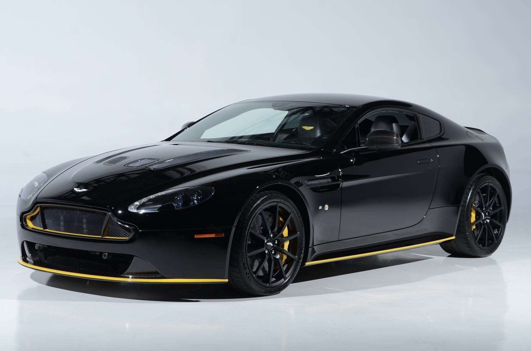 A sleek black sports car with yellow accents on the grille, wheels, and side skirts, parked on a plain white background.