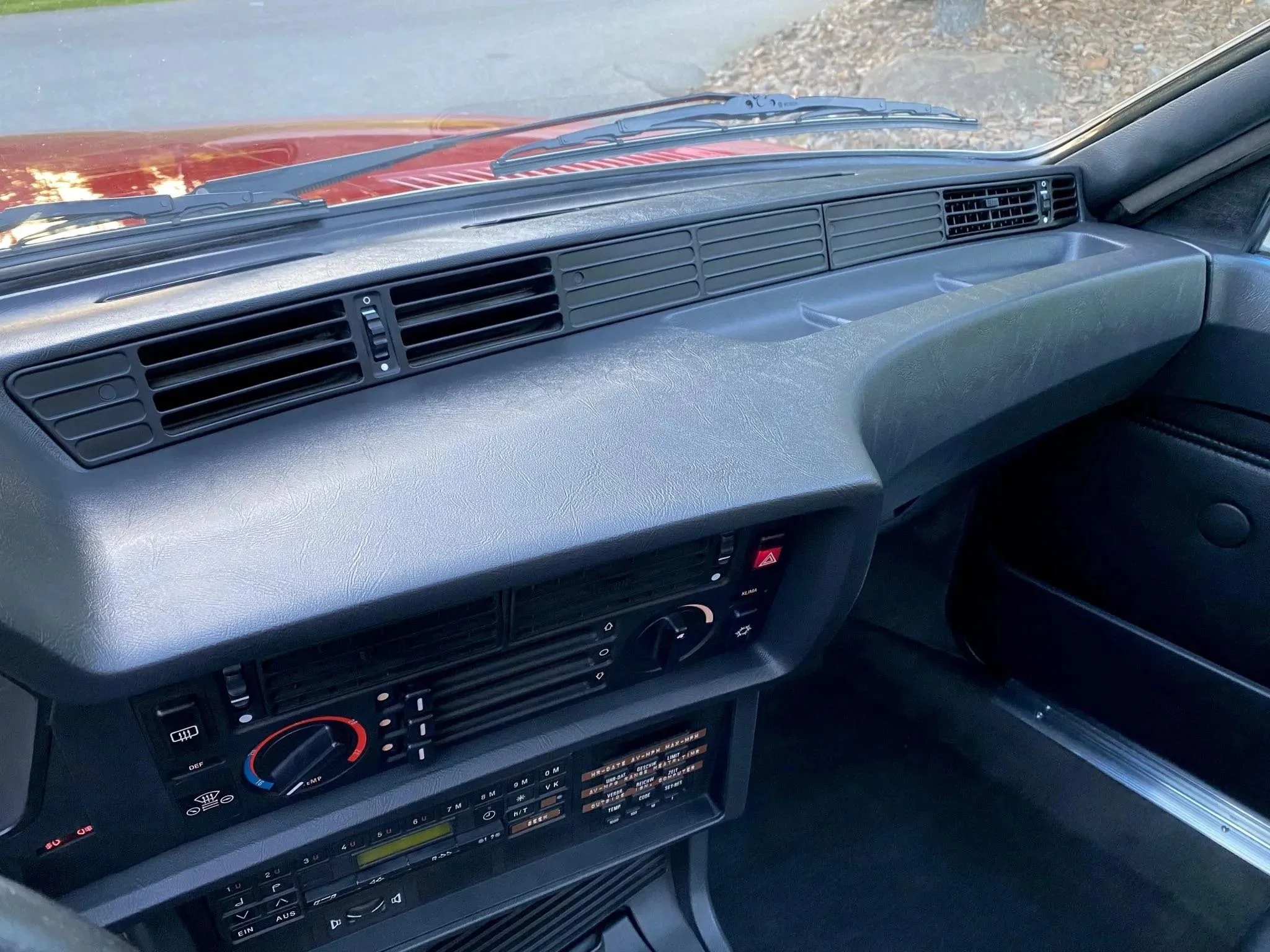 Dashboard of a vintage vehicle with air vents, climate controls, and a radio. The dashboard is gray with a steering wheel on the left.
