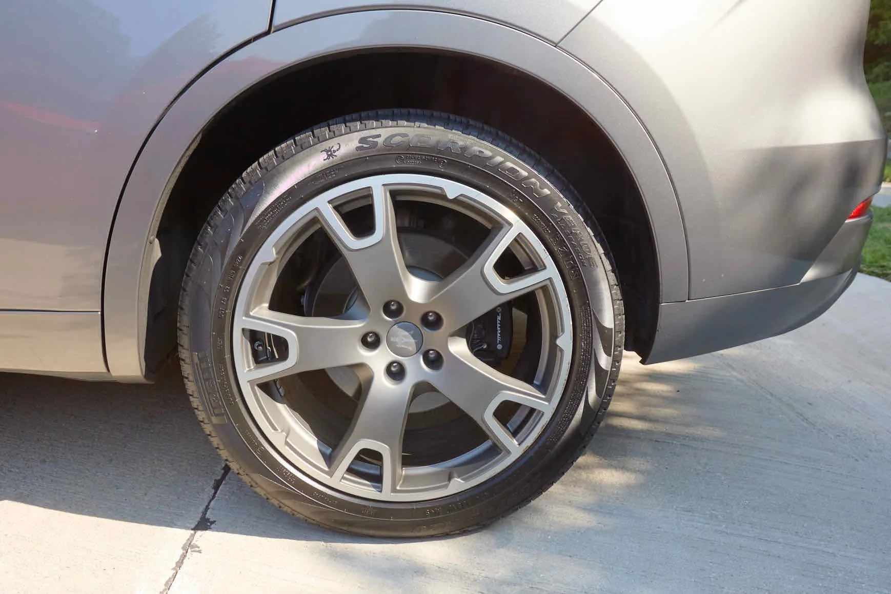 Close-up of a car's front wheel showing tire and alloy rim, parked on a concrete driveway.