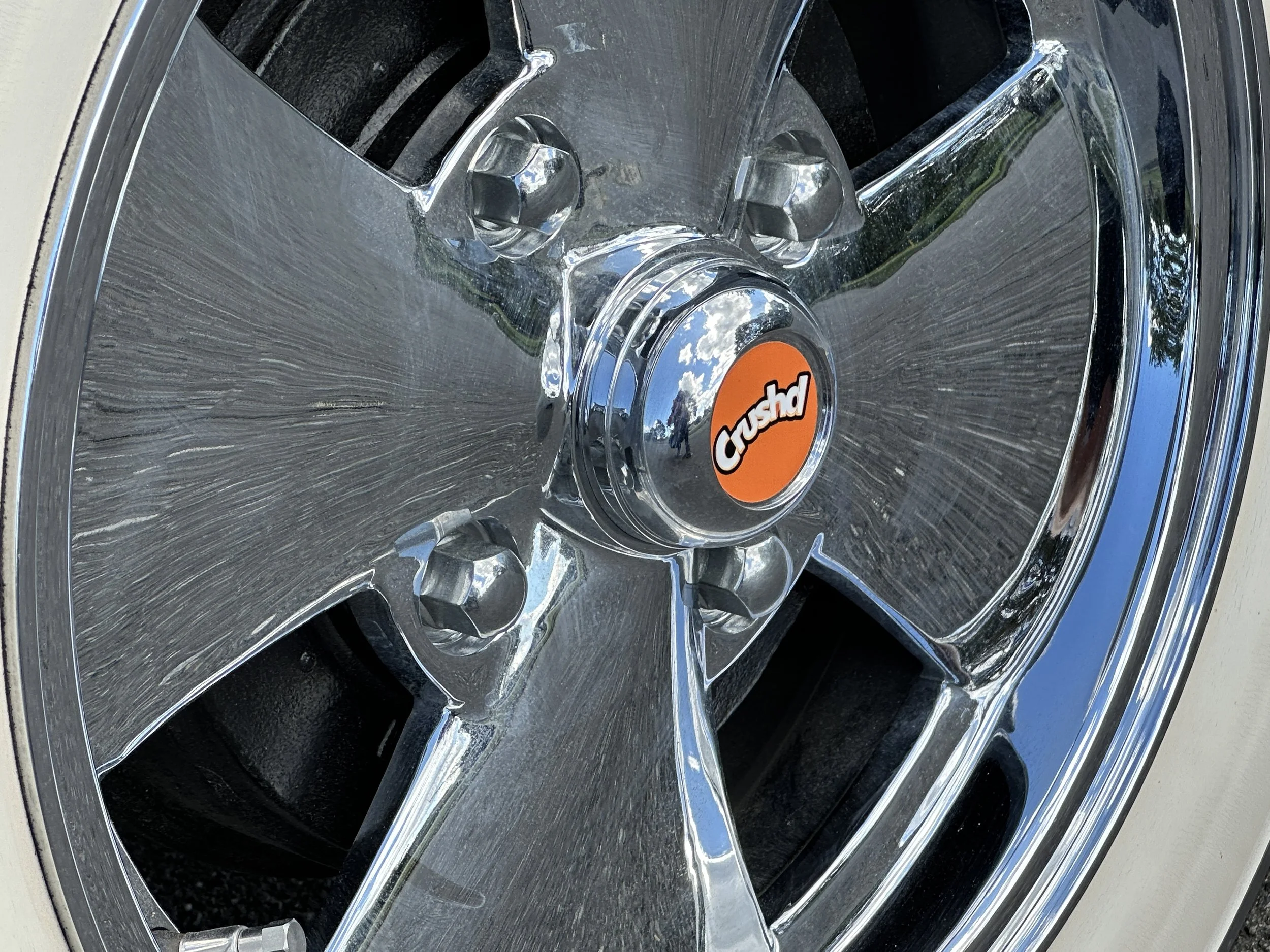 Close-up of a shiny chrome car wheel with a center cap labeled 'Crushed' in orange and black.