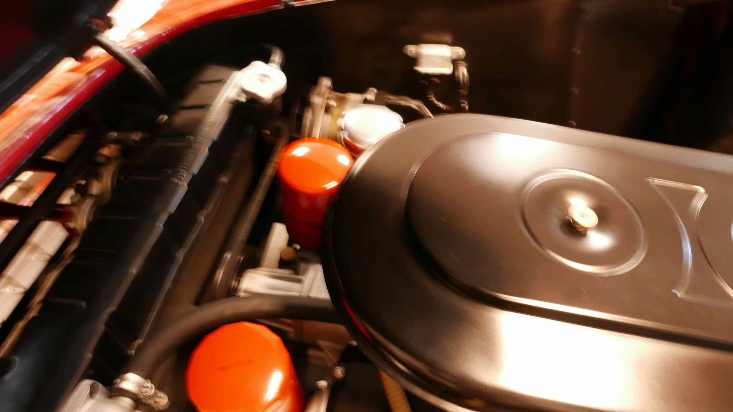 Close-up of a vintage car engine showing various engine components, including a black carburetor, orange oil filters, and metal piping.