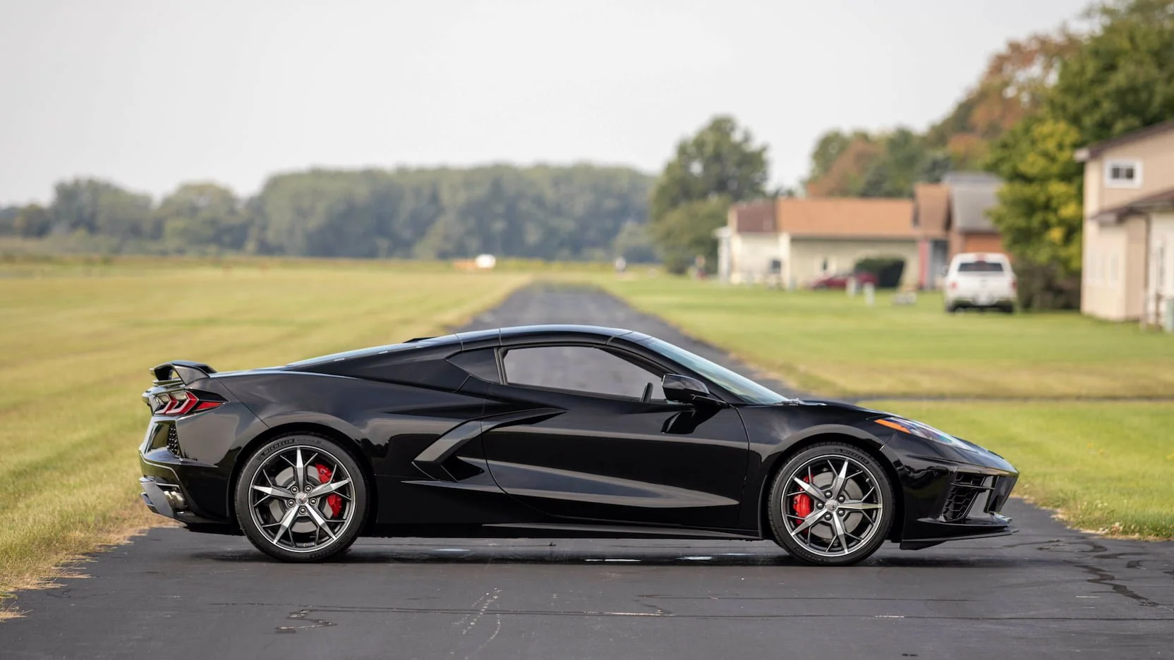 Black sports car parked on a paved driveway with grass and suburban houses in the background.