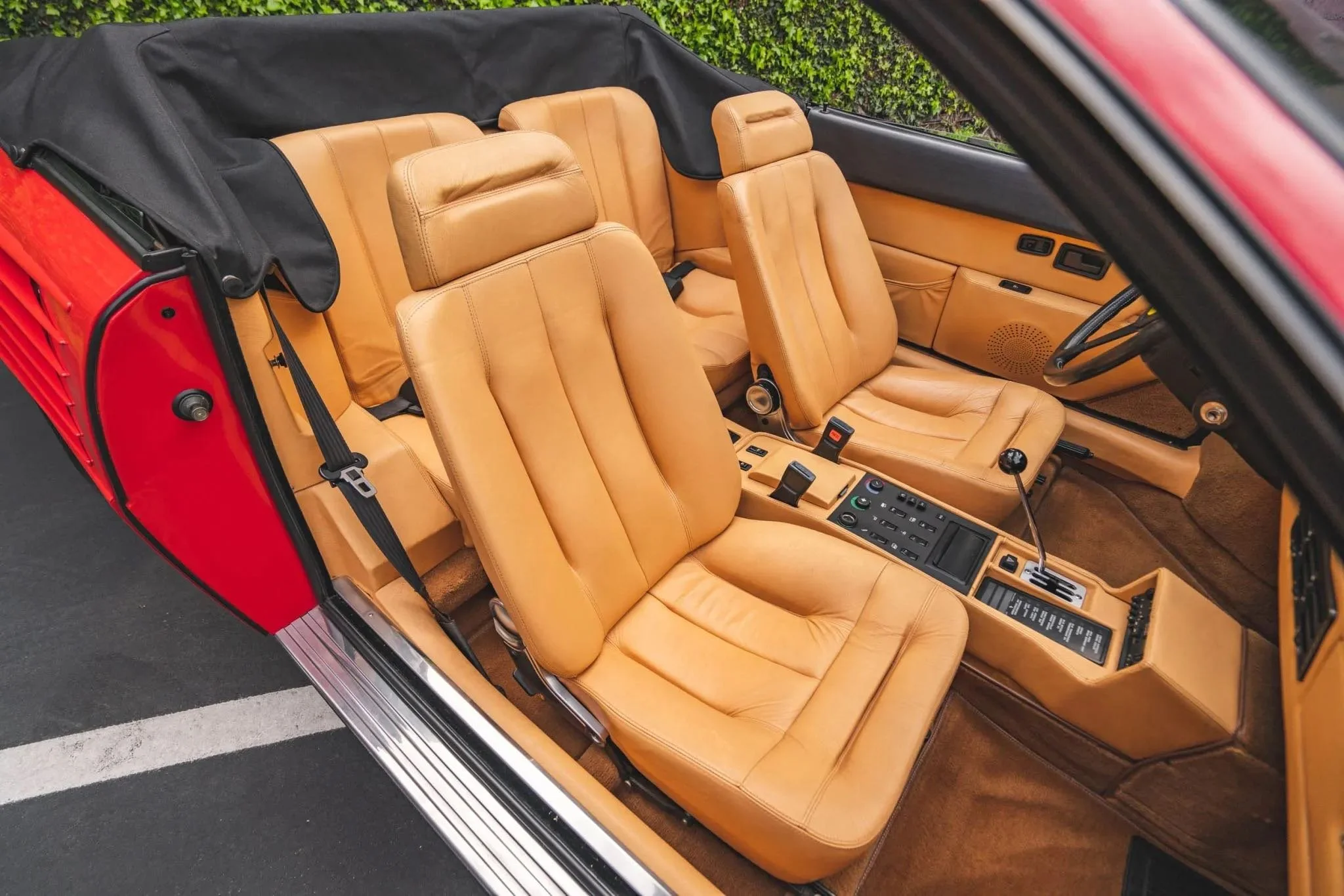 Interior of a vintage car with tan leather seats, black roof cover, and dashboard with controls and gear shift.