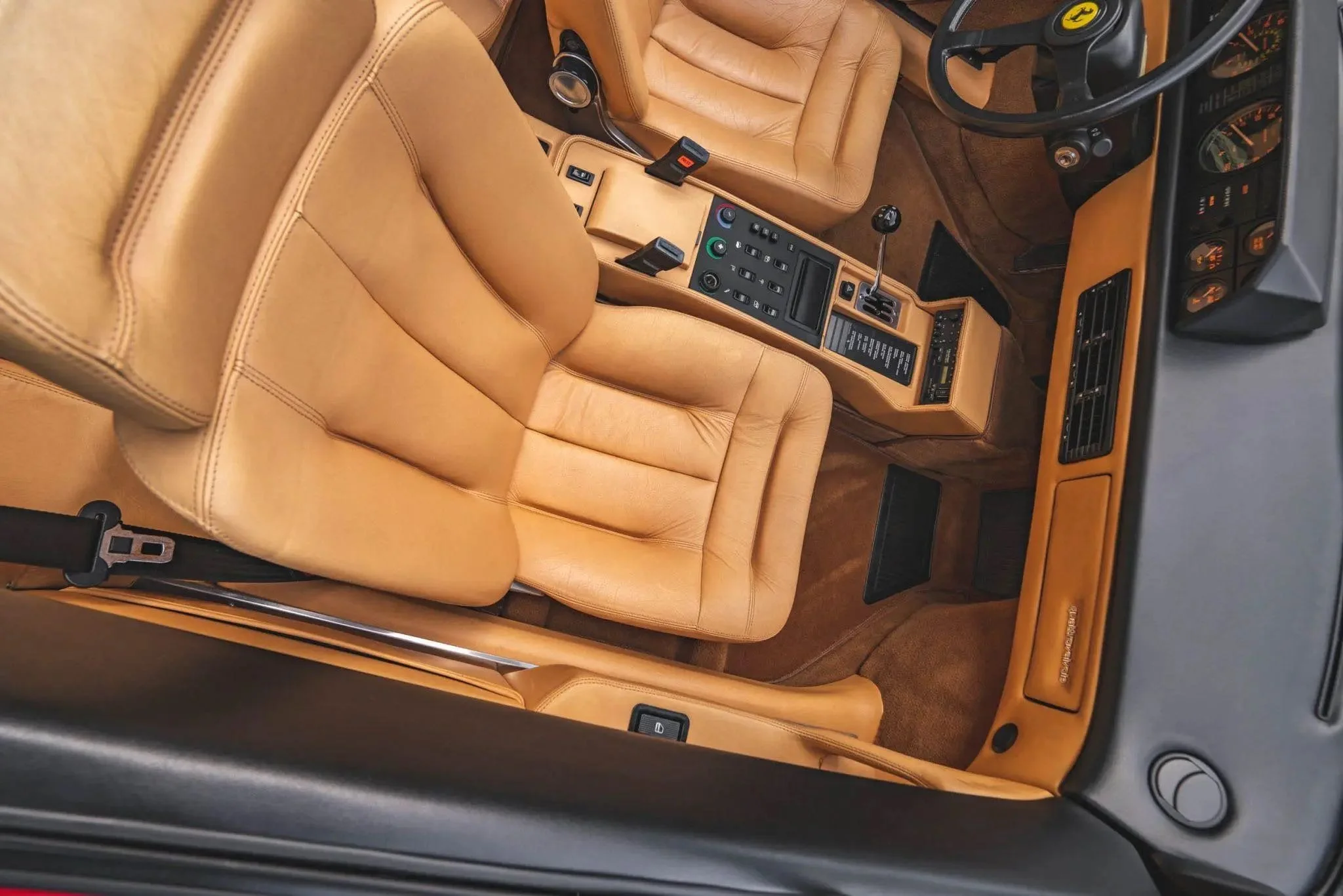 Interior of a vintage car showing tan leather seats, a dashboard, and a center console with various control switches, a gear shift, and an air vent.