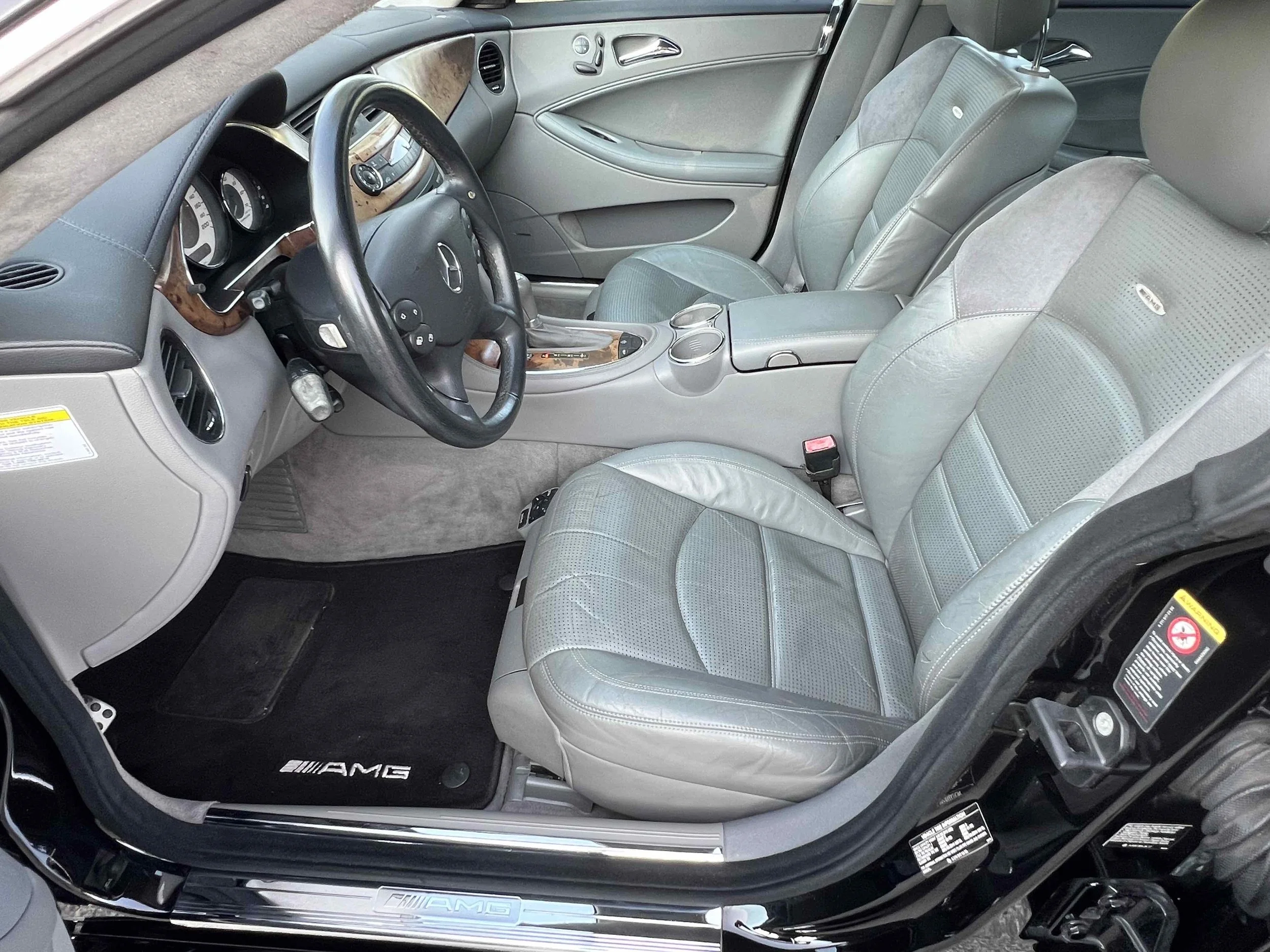 Interior of a Mercedes-Benz AMG car with grey leather seats, steering wheel, dashboard, and black AMG floor mat.