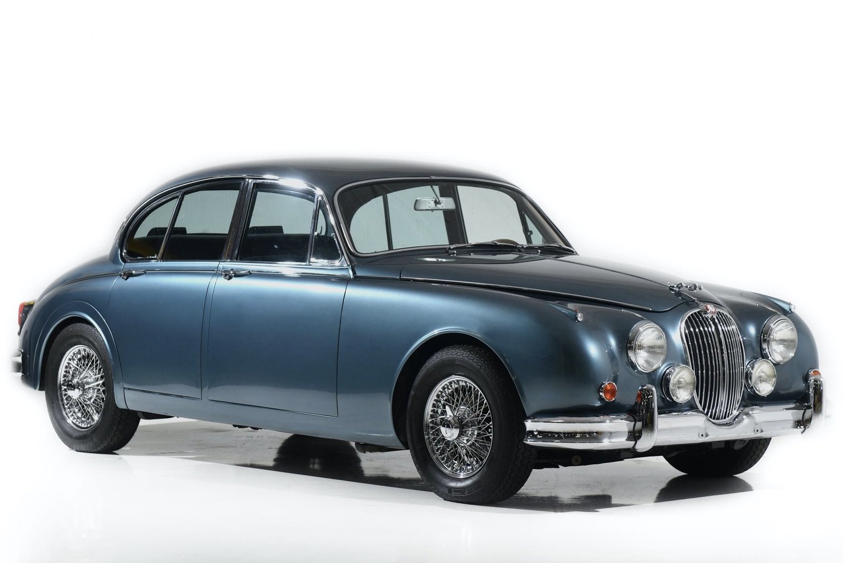 Classic vintage blue car with a rounded body and chrome wire wheels, featuring four headlights and a prominent grille.