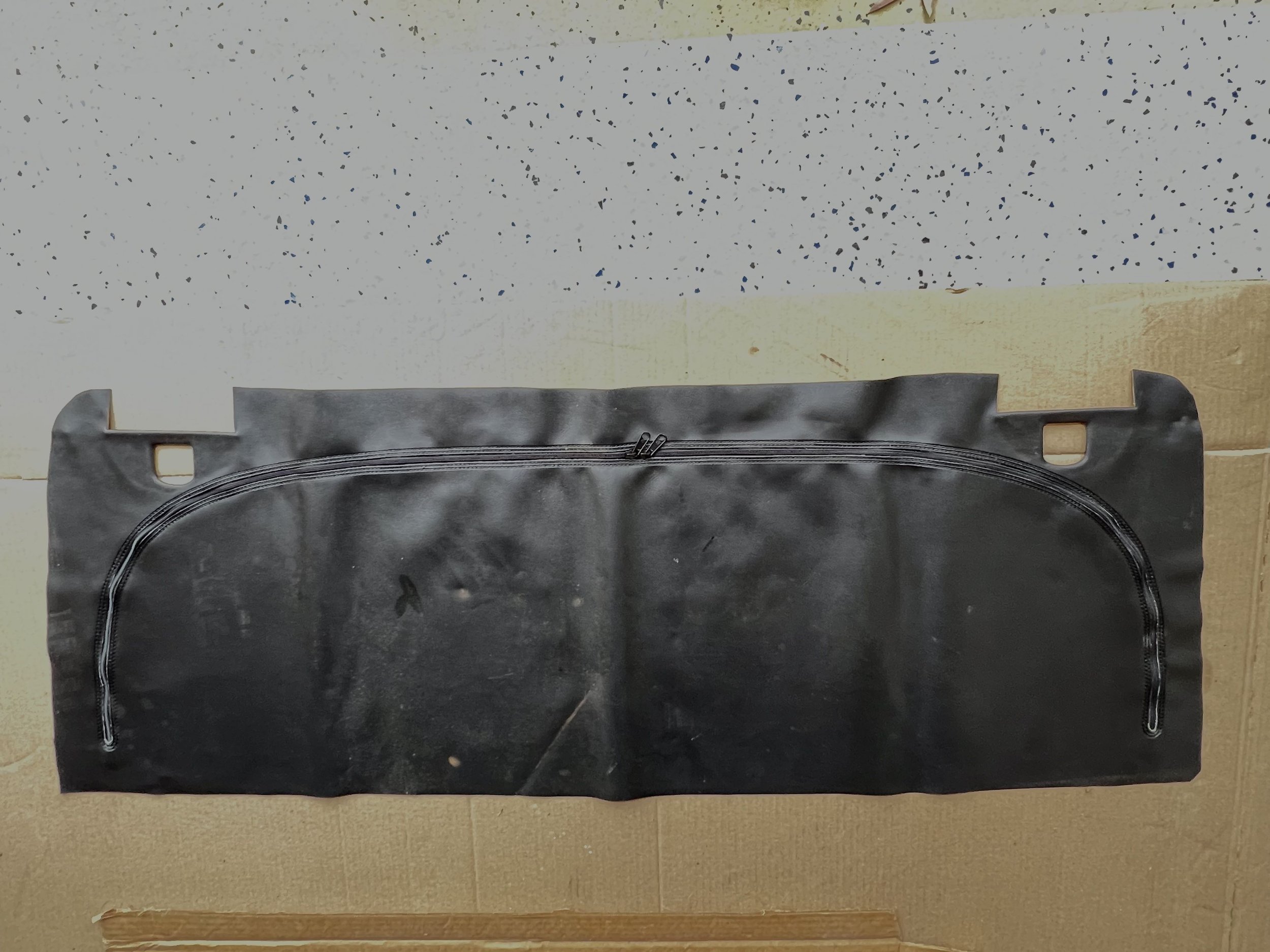 Black rubber car trunk seal with a curved zipper on a cardboard surface.