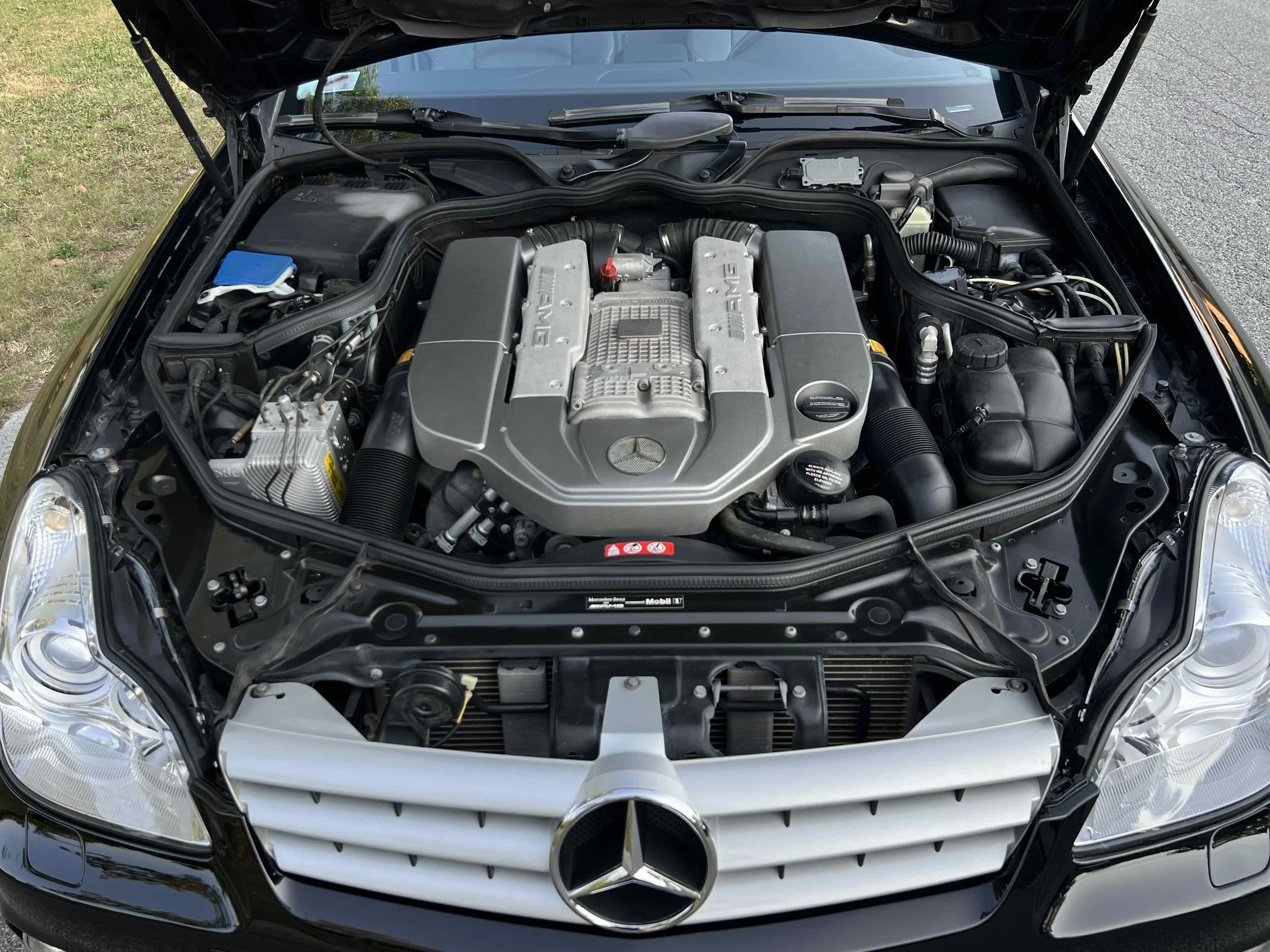 Front view of a Mercedes-Benz with the hood open, showing the engine bay with AMG branding on the engine cover.