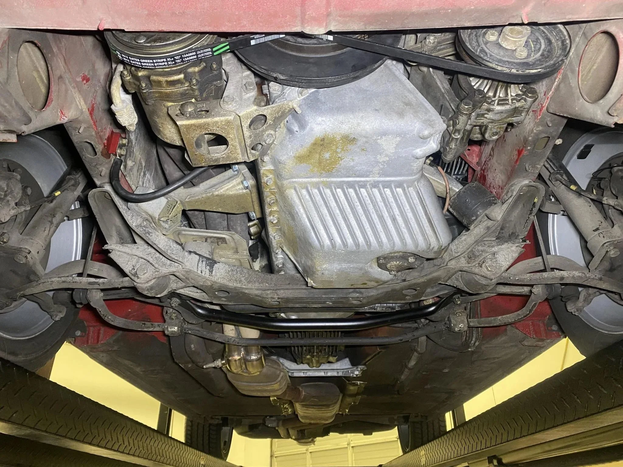 View of the underside of a vehicle's engine compartment with various mechanical components, belts, and parts visible.