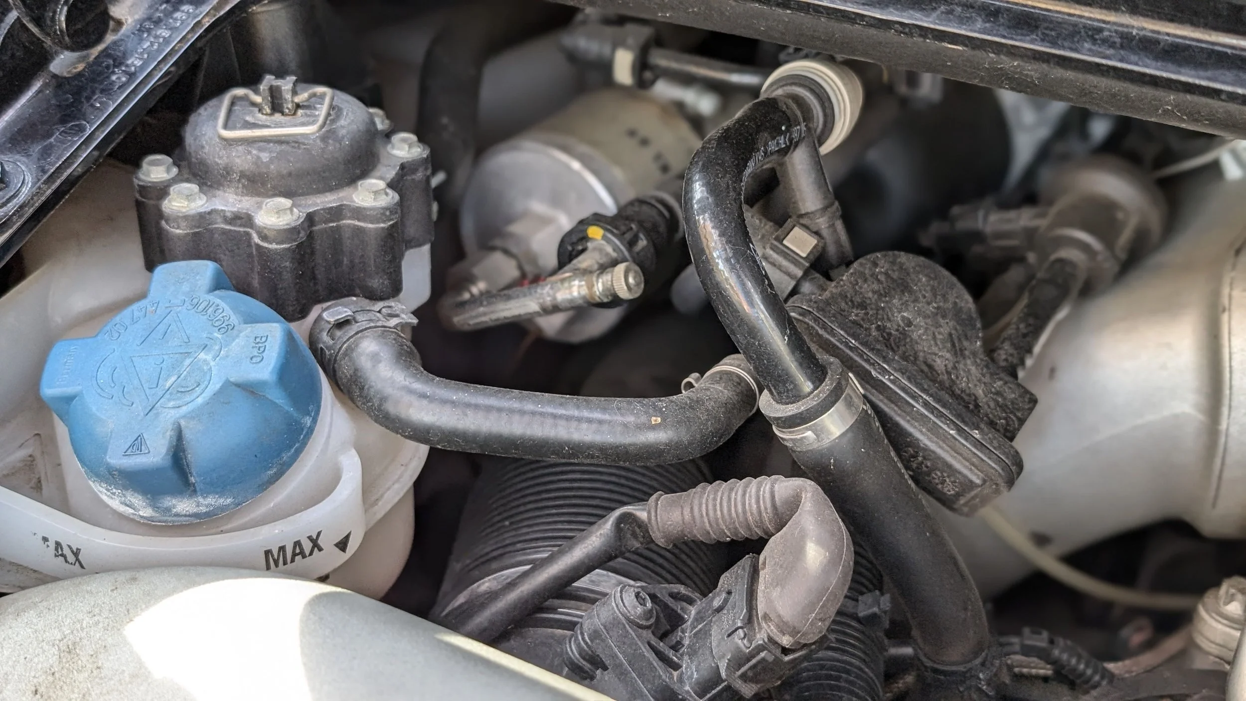 Close-up of a car engine showing various hoses, caps, and components with a dirty appearance.