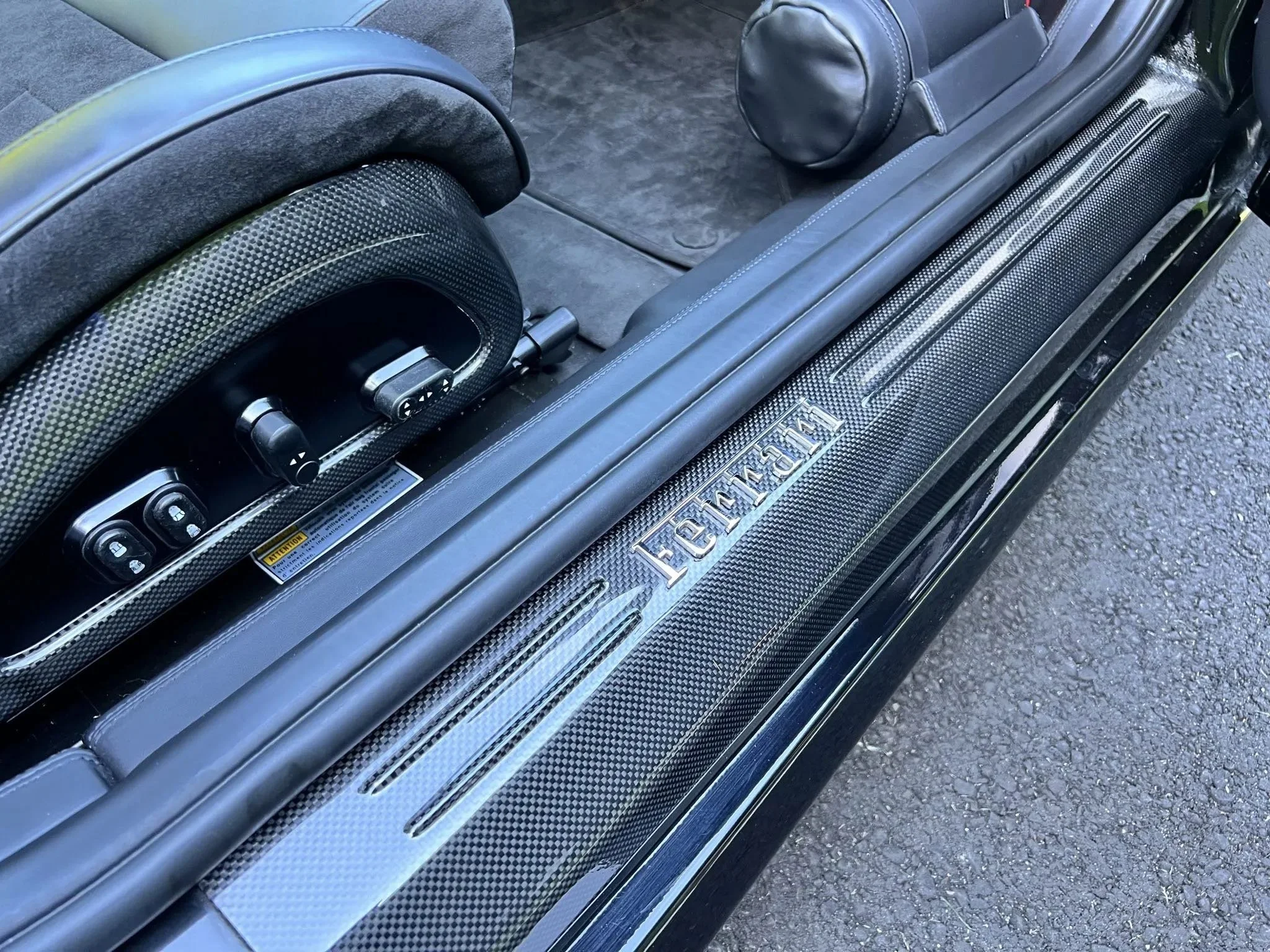 Close-up of the interior of a McLaren vehicle, showing carbon fiber trim and part of the door sill with the McLaren logo.