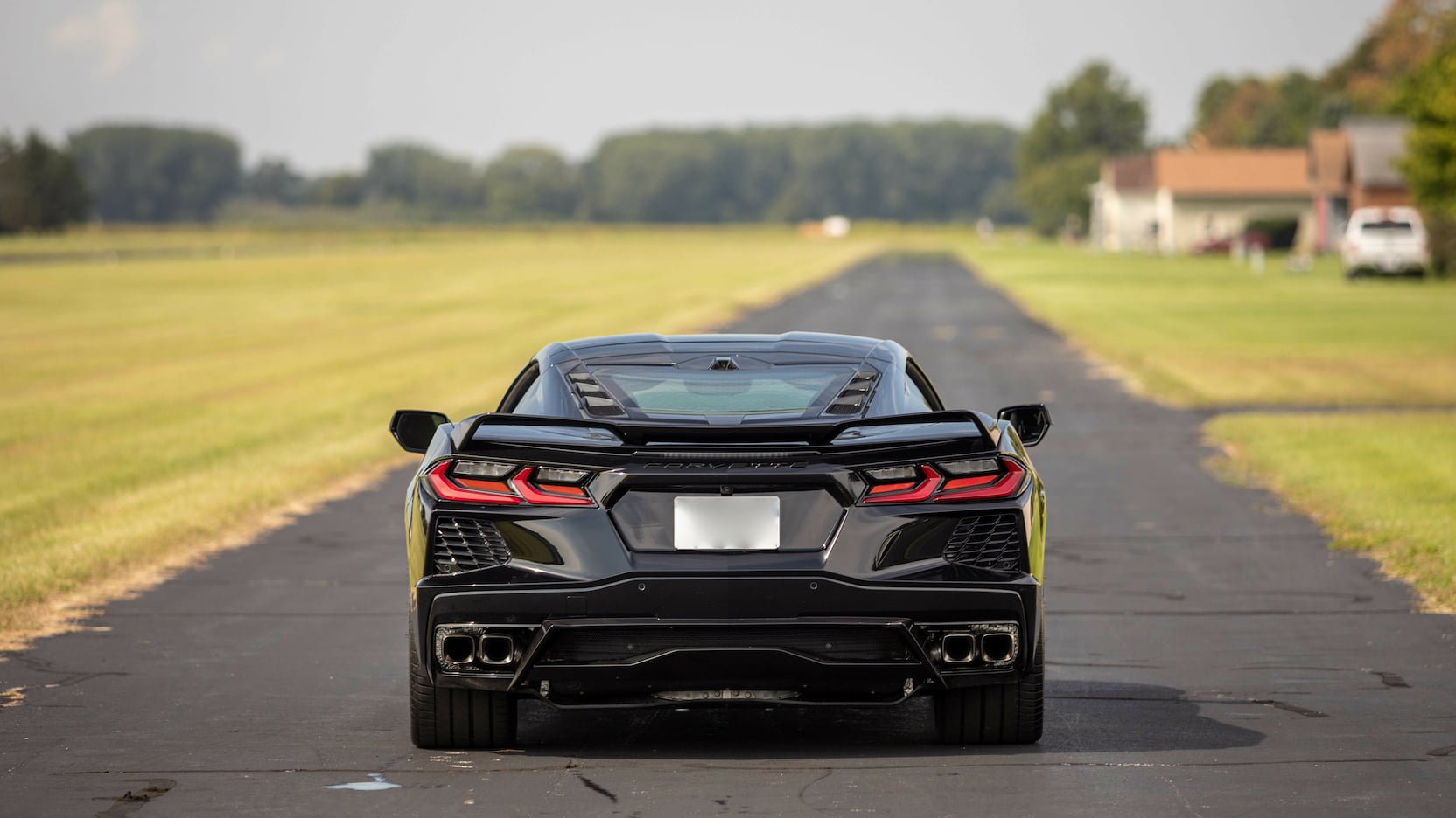 Black sports car on an empty rural road with houses and trees in the background.