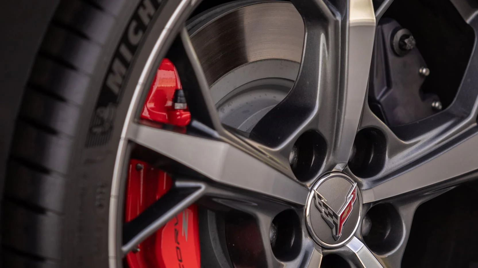 Close-up of a Chevrolet Corvette wheel with a red brake caliper visible behind the black rim with a Chevrolet Corvette logo in the center