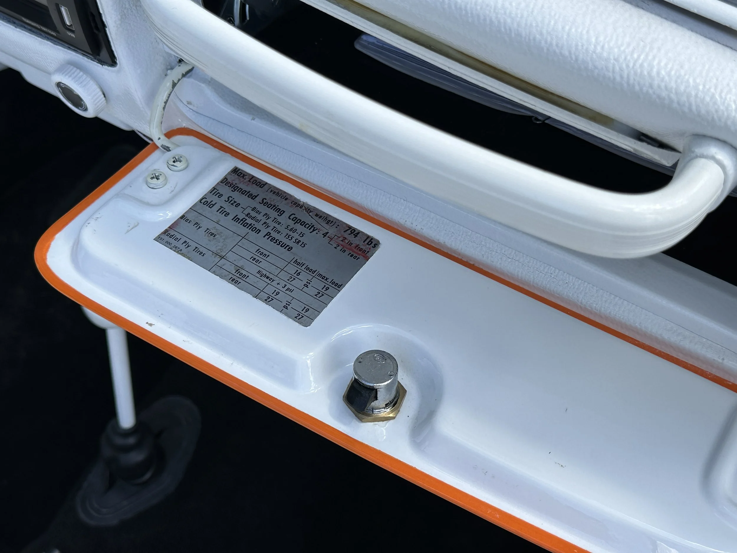Close-up of a vehicle's tire information and load capacity plate mounted inside the door frame, with a white lining and a bolt nearby.