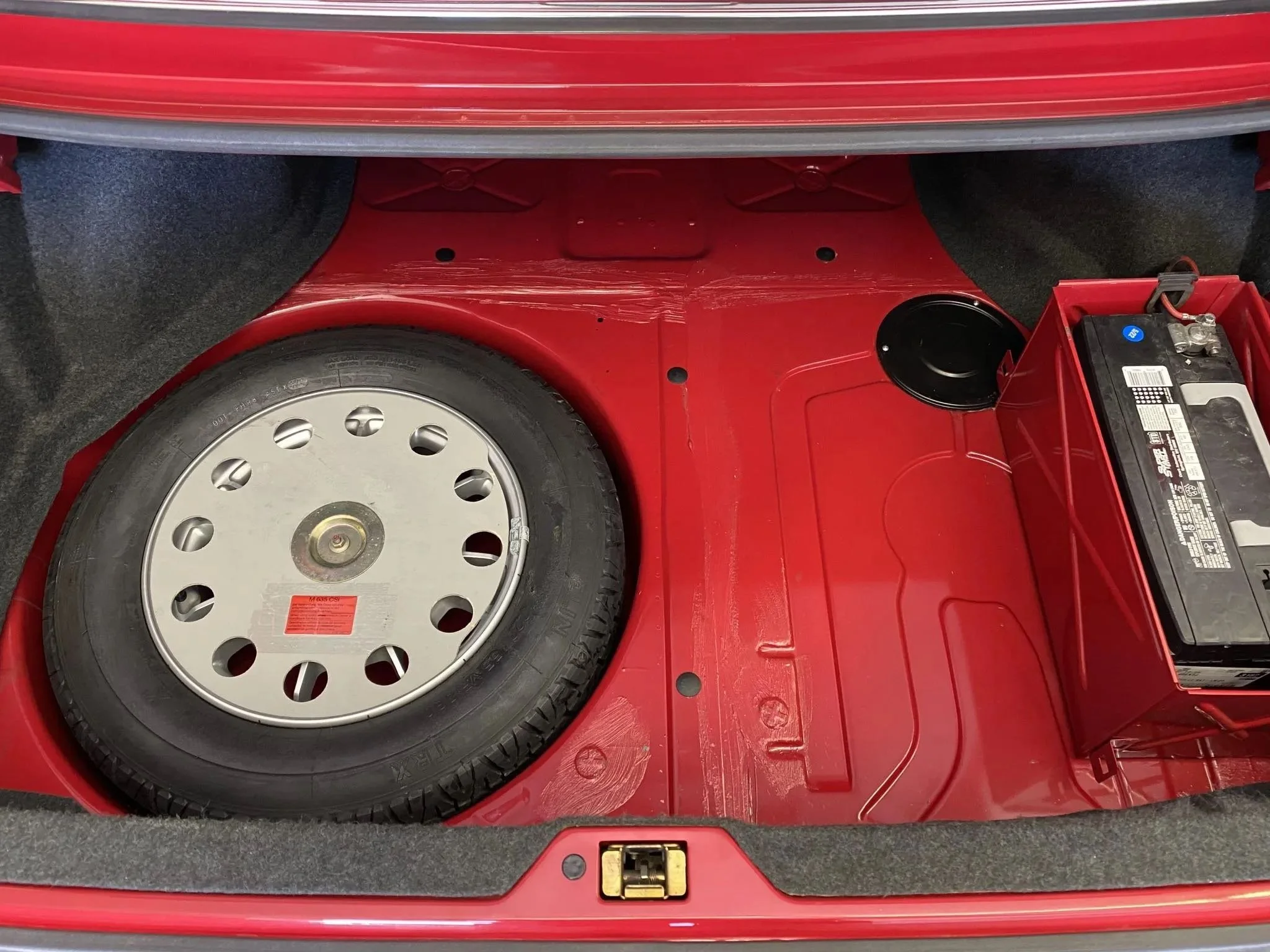 Spare tire and car battery in the trunk of a red vehicle.
