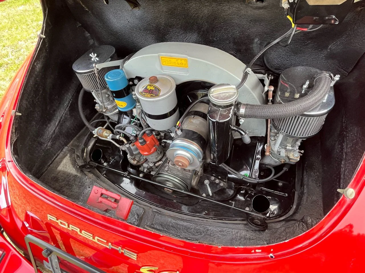 Engine compartment of a classic red Porsche with visible air filters, a fuel filter, and various engine components.