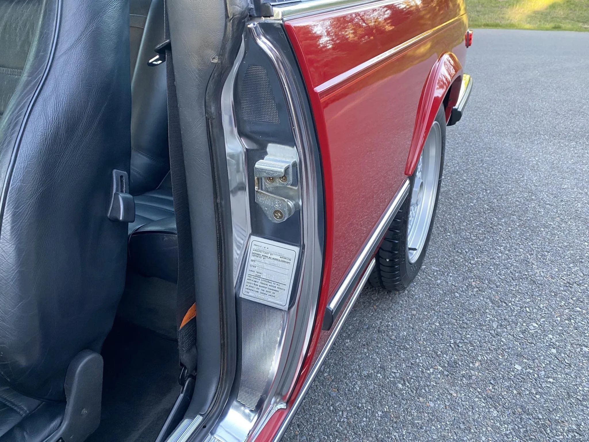 Rear side door area of a red vintage car showing the door latch, motor, and a portion of the interior with a black seat.