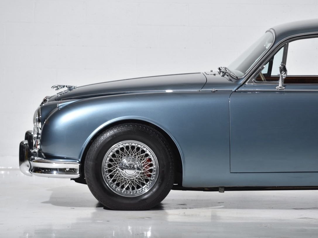 Close-up of a vintage blue luxury car showcasing the front wheel, fender, and partially visible door, set against a plain white background.