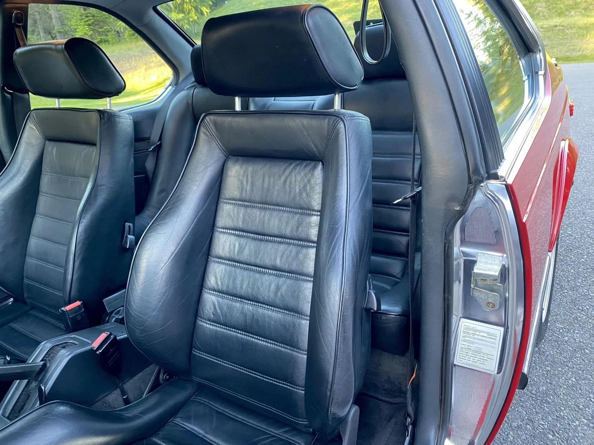 The interior of a car showing three rows of black leather seats, with view from the open rear door showing the seats and a grassy outdoor background.