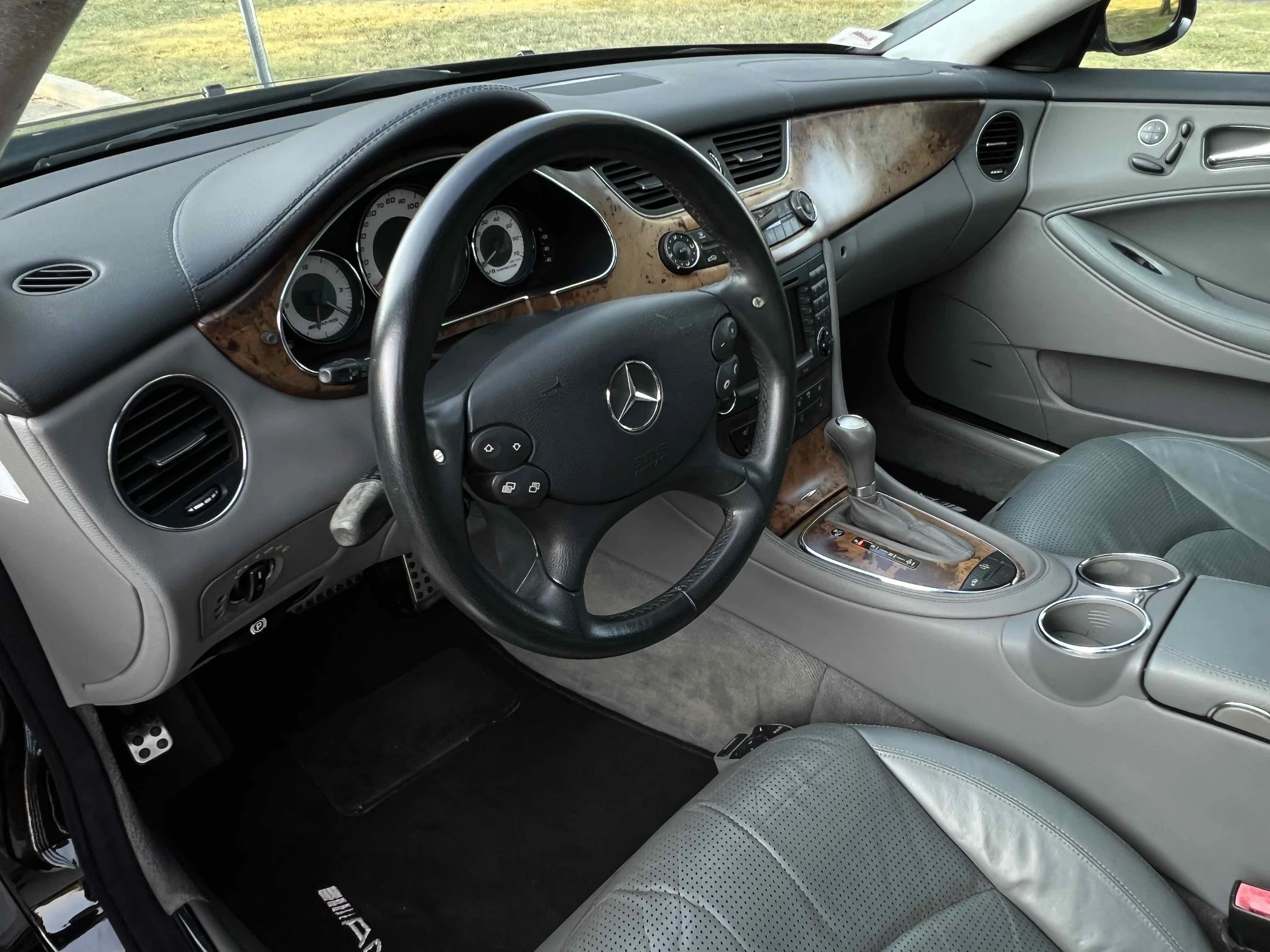 Interior of a luxury car with a black leather steering wheel, wooden dashboard and center console, and grey leather seats.