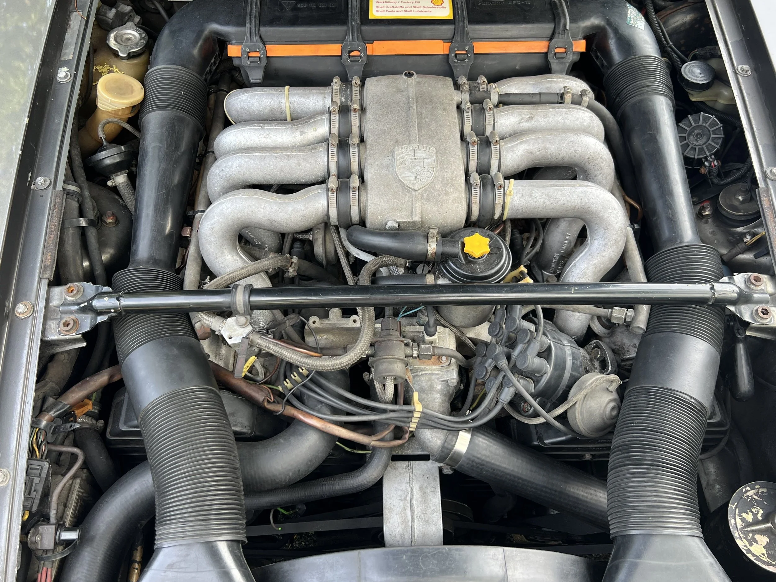 Front view of a Porsche car engine with various pipes, hoses, and mechanical components.