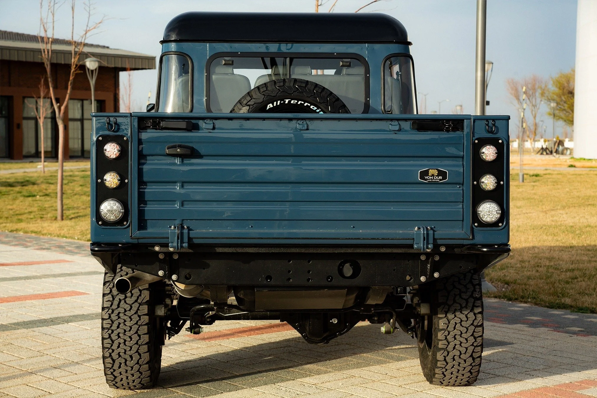 Front view of a vintage blue Land Rover with a spare tire on the back, parked on a paved area