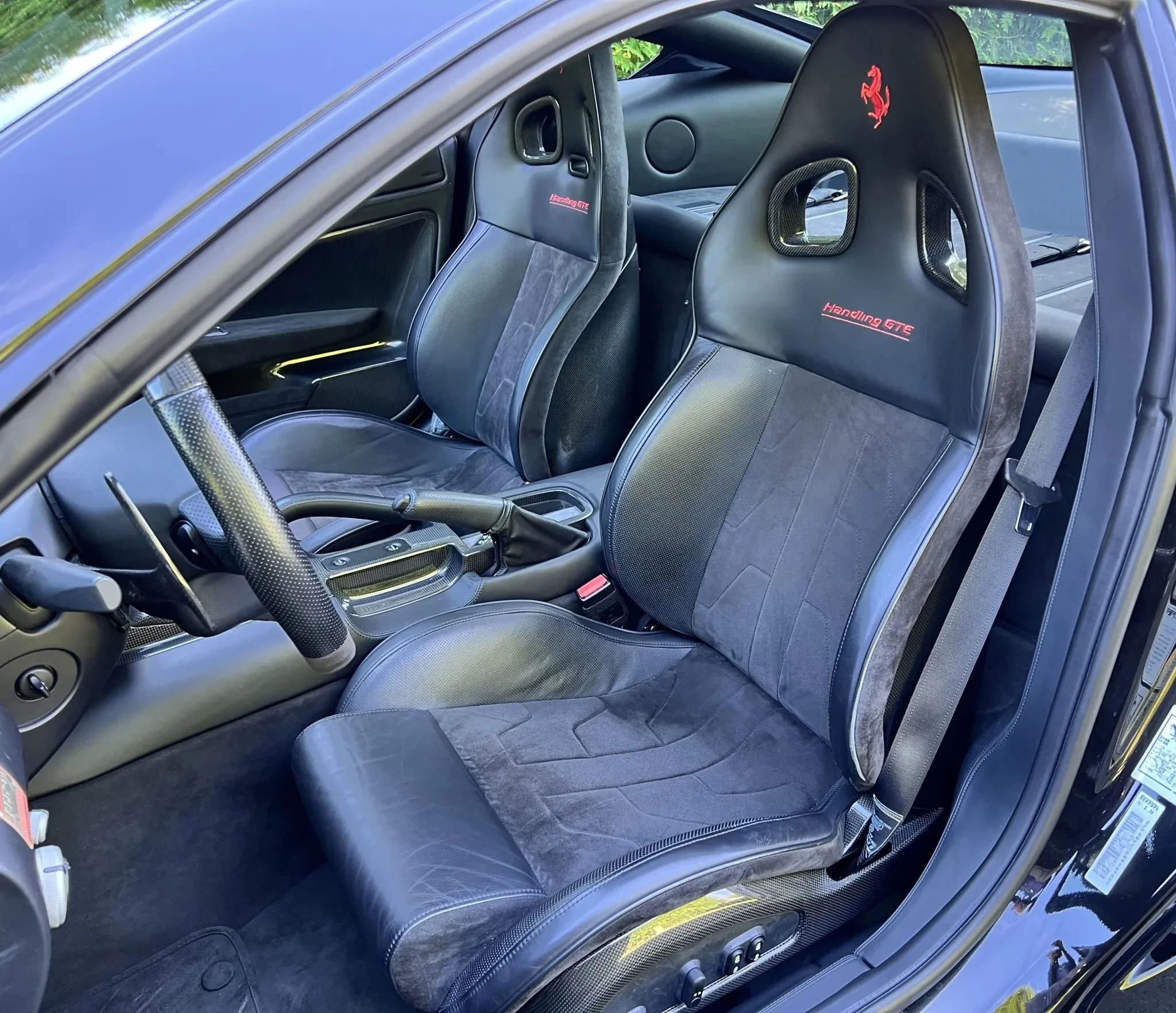 The interior of a sports car showing black racing seats with the Ferrari logo and 