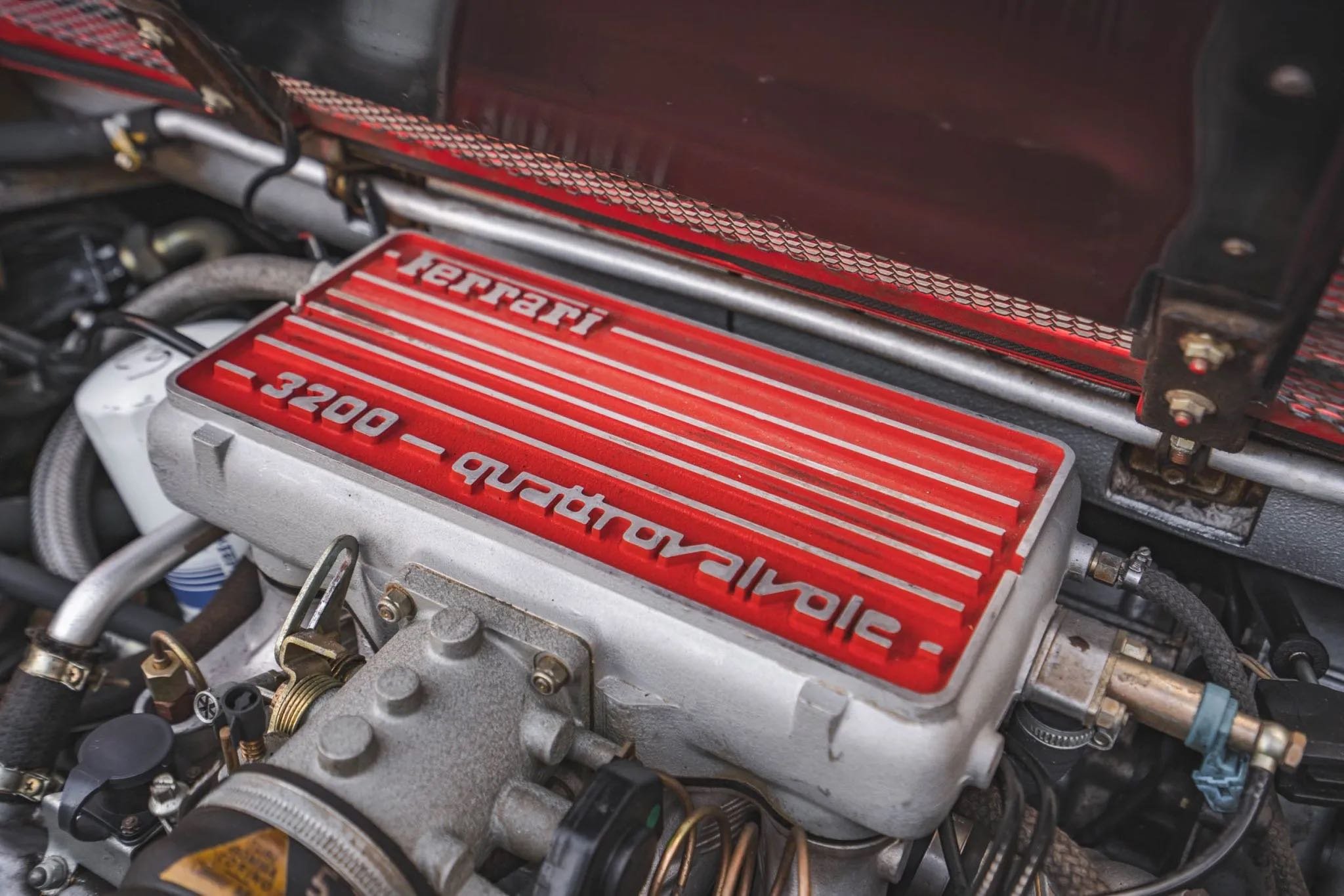 Close-up of a Ferrari engine with a red valve cover that has 'Ferrari' and '3200 - quattrovalve' written on it.
