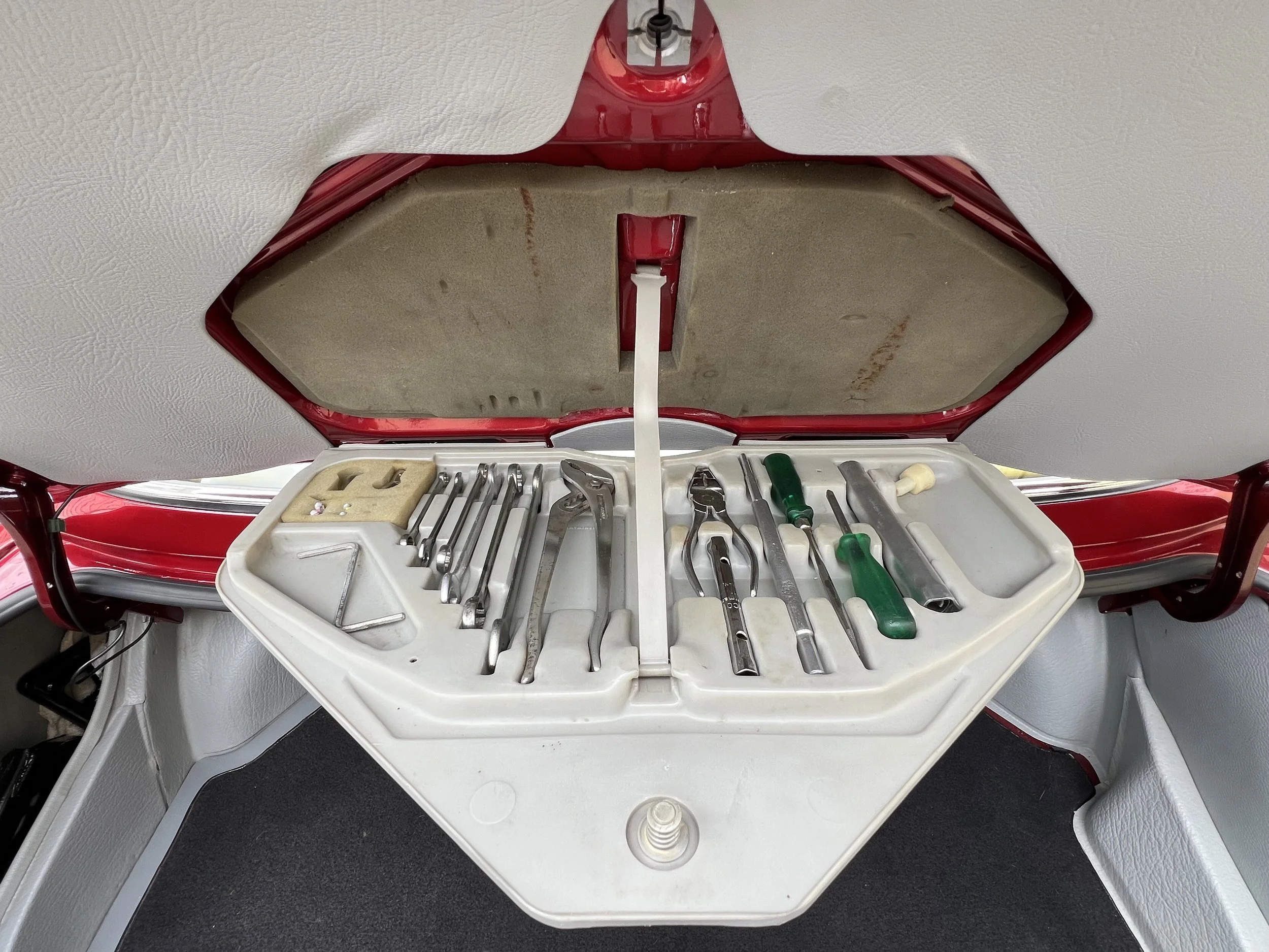 A 1977 BMW 630 csi tool kit with various metal and plastic tools organized inside a white plastic container.