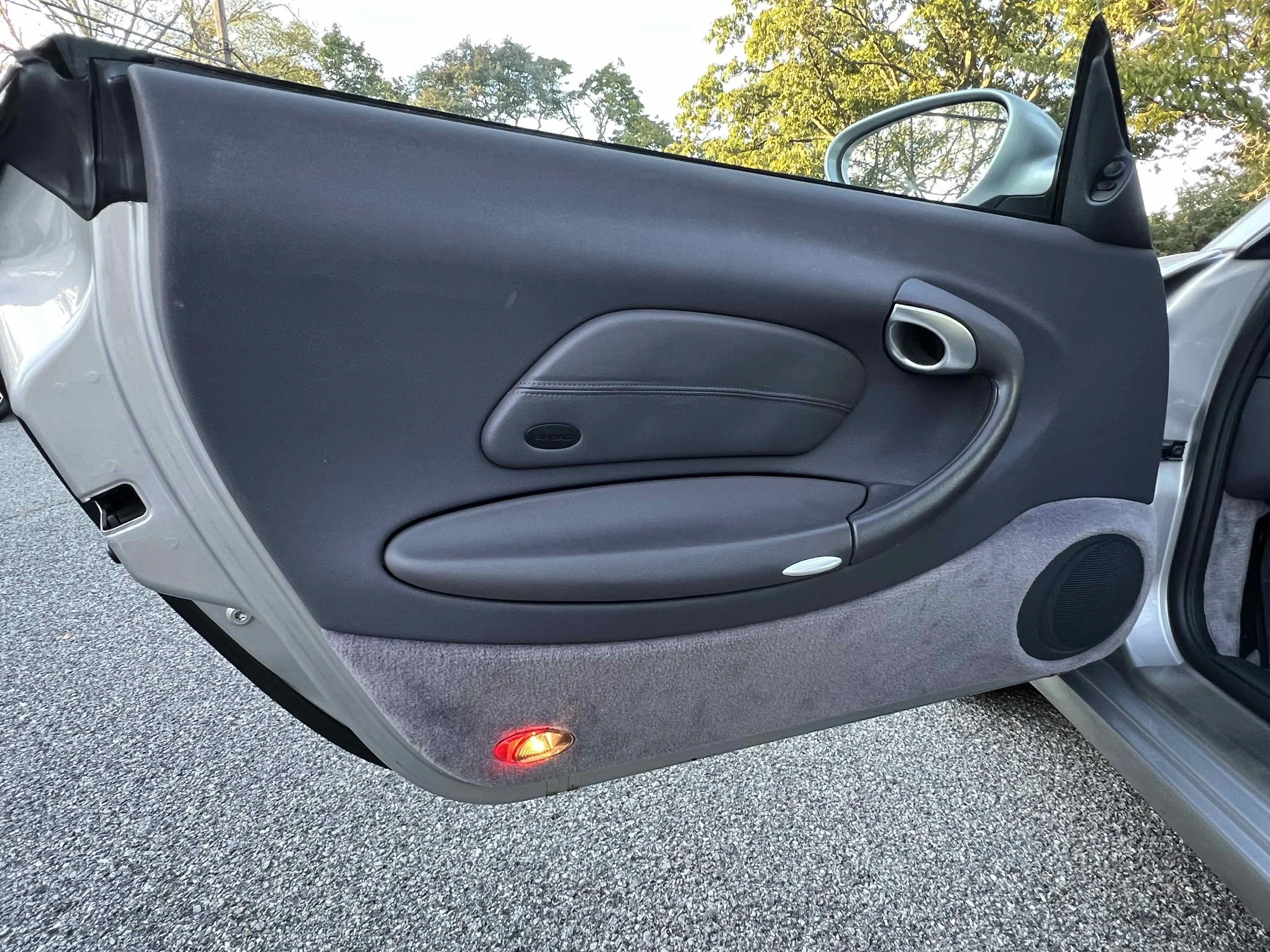 Interior of a car door showing black upholstery, a door handle, speaker, and a red light at the bottom.