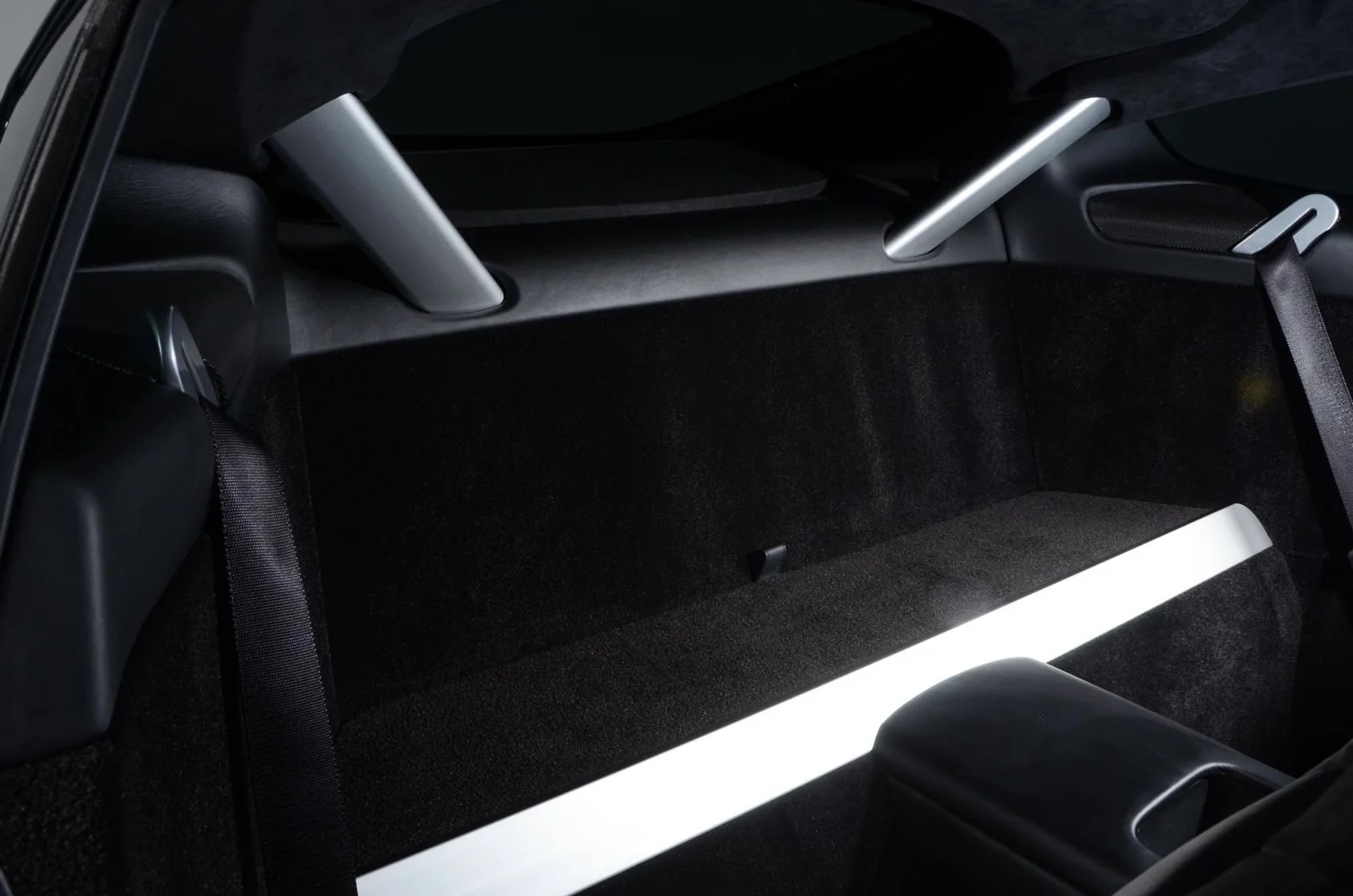 The trunk interior of a car, featuring a black carpeted storage area with metallic support bars and a white ambient light strip.