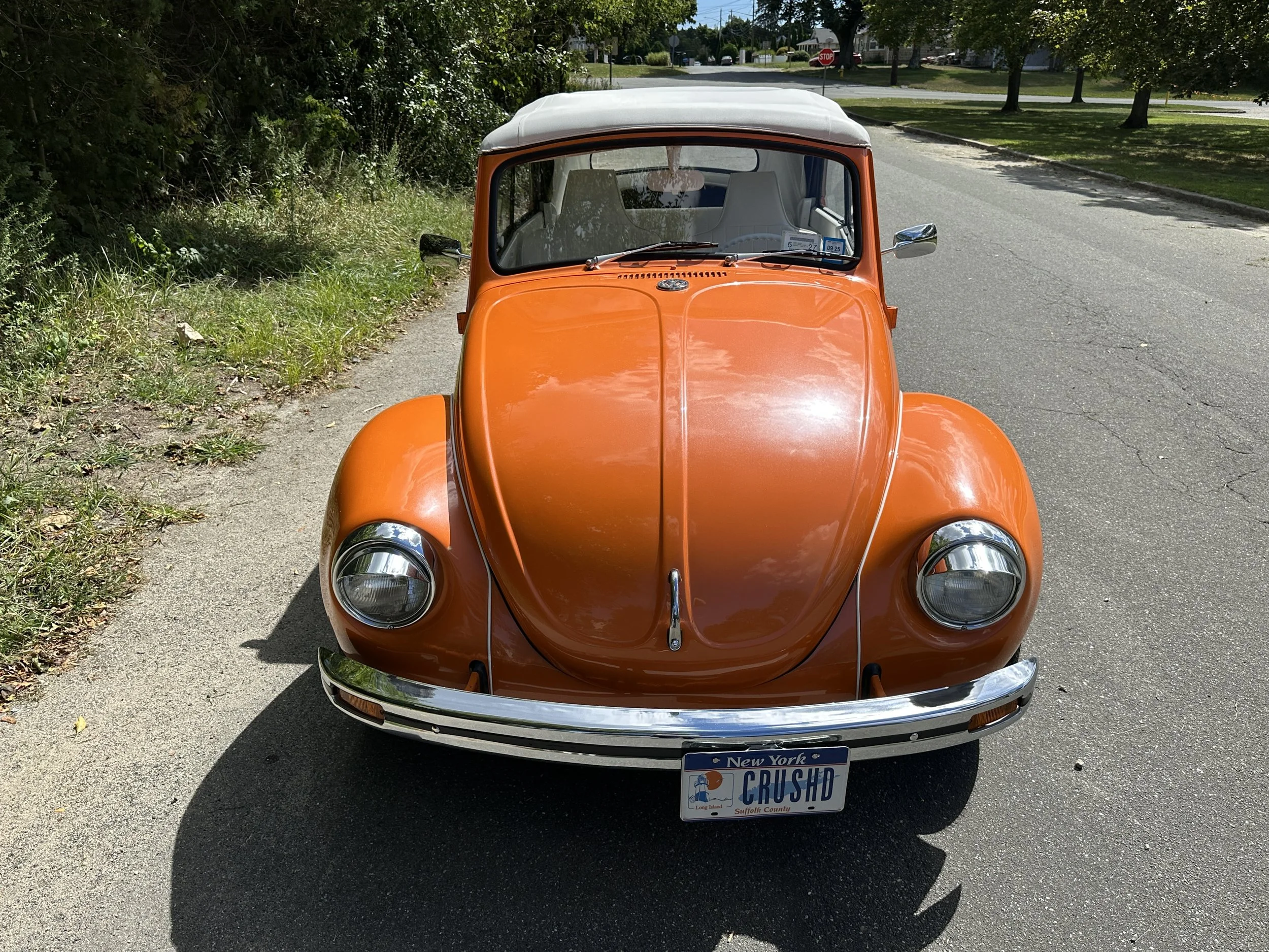 Front view of an orange vintage Volkswagen Beetle parked on the side of a residential street.